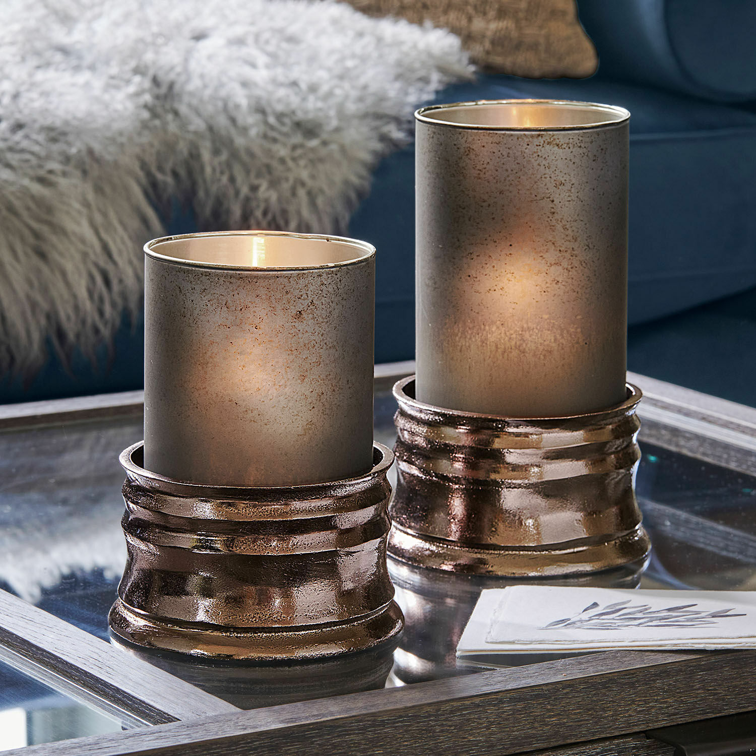 Zwei dekorative Windlichter aus Glas und kupferfarbenem Metall auf einem Glastisch im Wohnzimmer