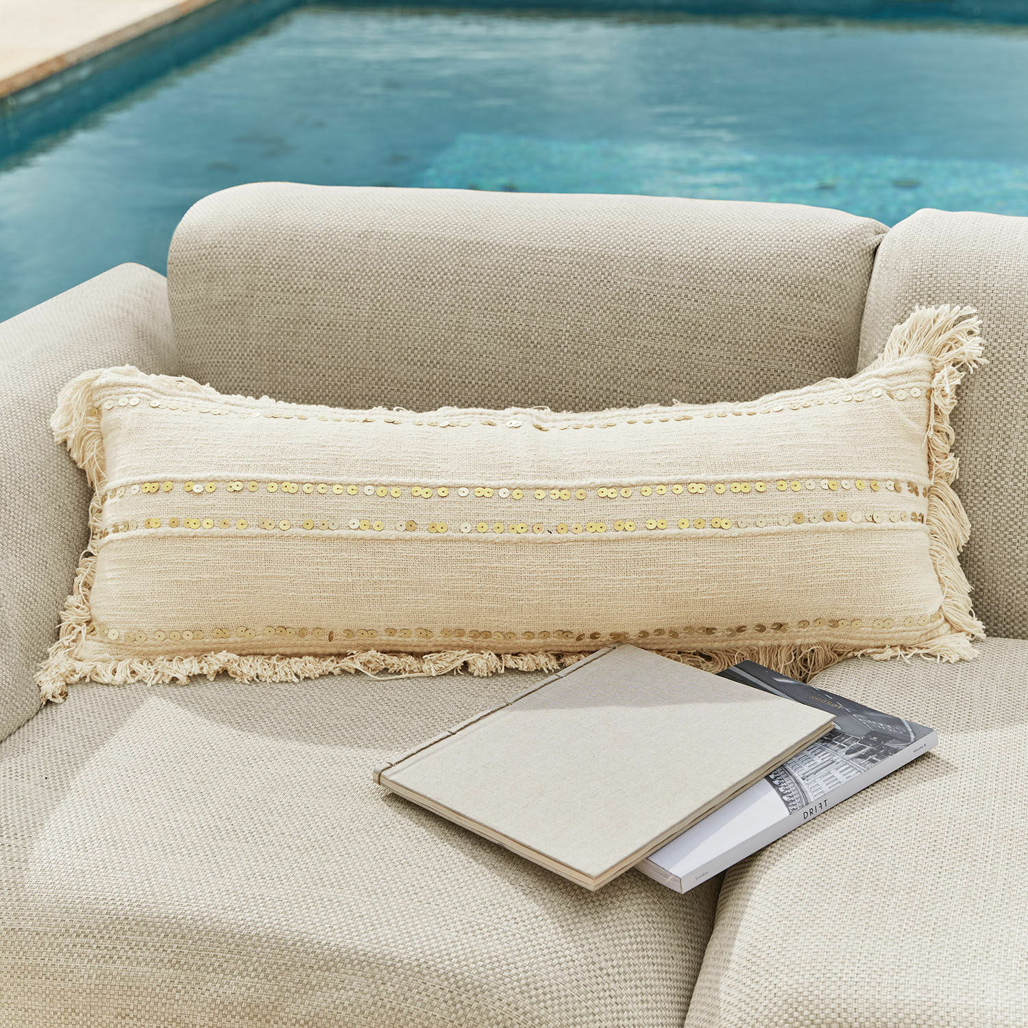 Kissen Rousseline Beige längliches Dekokissen mit Pailletten und Fransen auf hellem Sofa am Pool