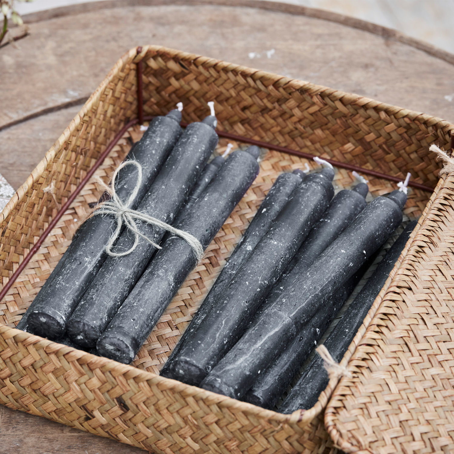 Set aus schwarzen Kerzen aus Wachs im geflochtenen Korb auf Holztisch