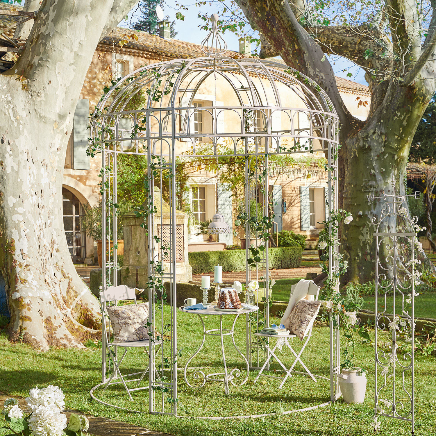 Pavillon Iolanda Weiße Metall-Gartenlaube mit Stühlen und Tisch auf Rasen, dekoriert mit grünem Efeu