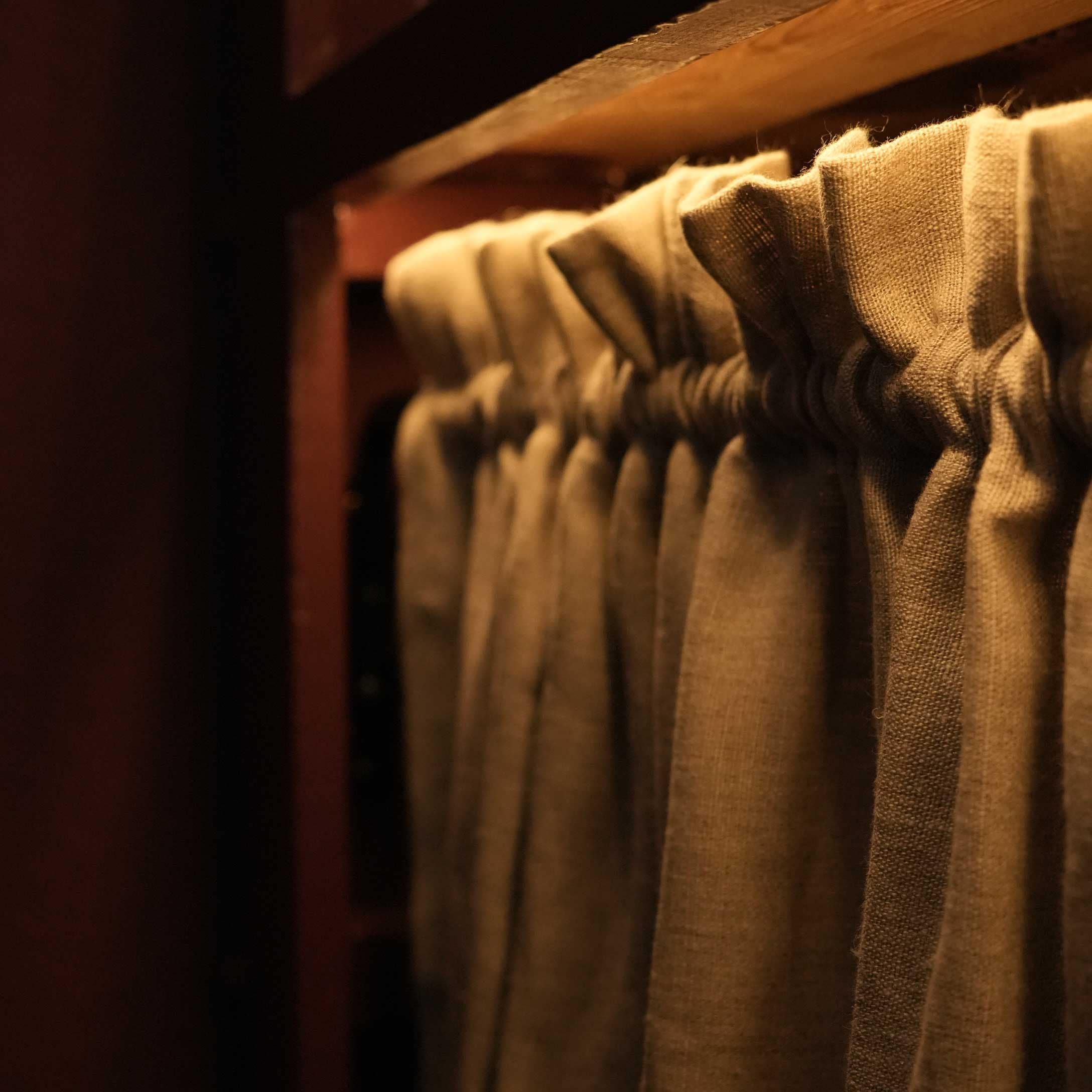 Beige Leinenvorhang mit Falten an einem Holzstangenhalter in warmem Licht