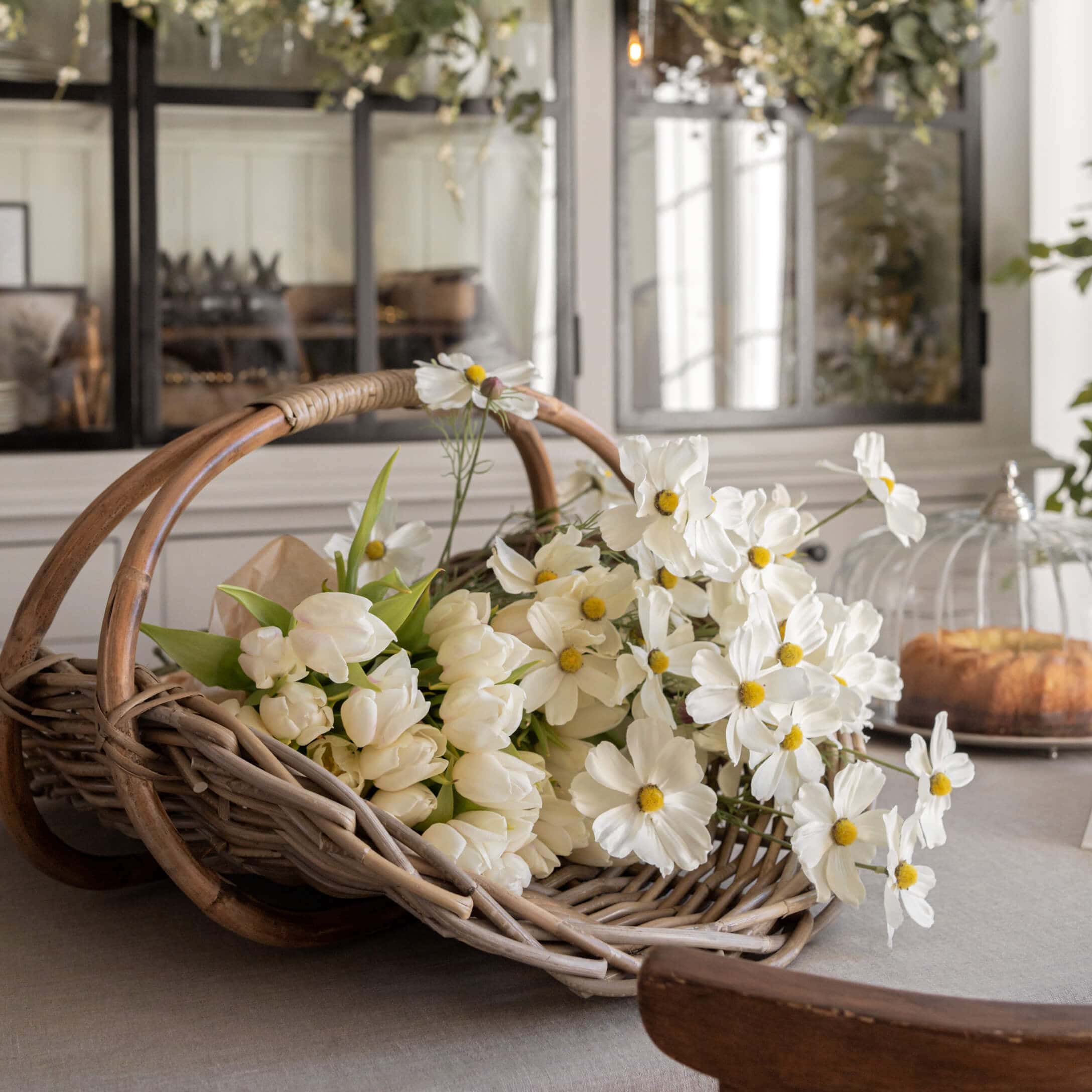 Wikliniger Korb mit weißen Tulpen und dekorativen Blumen auf Tisch in hellem Raum