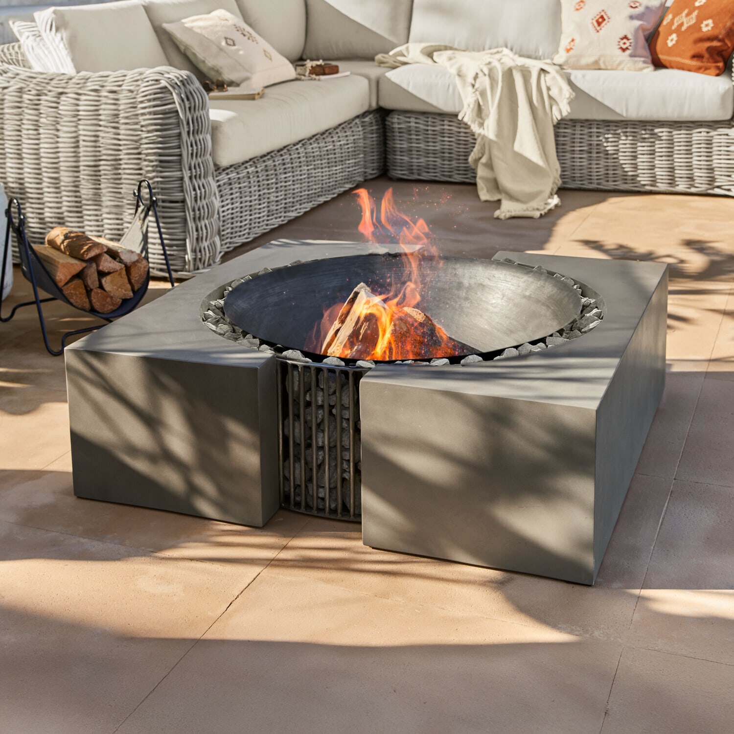 Feuerstelle Charonville Modernes Feuerstelle aus schwarzem Metall mit Steinen auf Terrasse neben Rattansofa mit Kissen