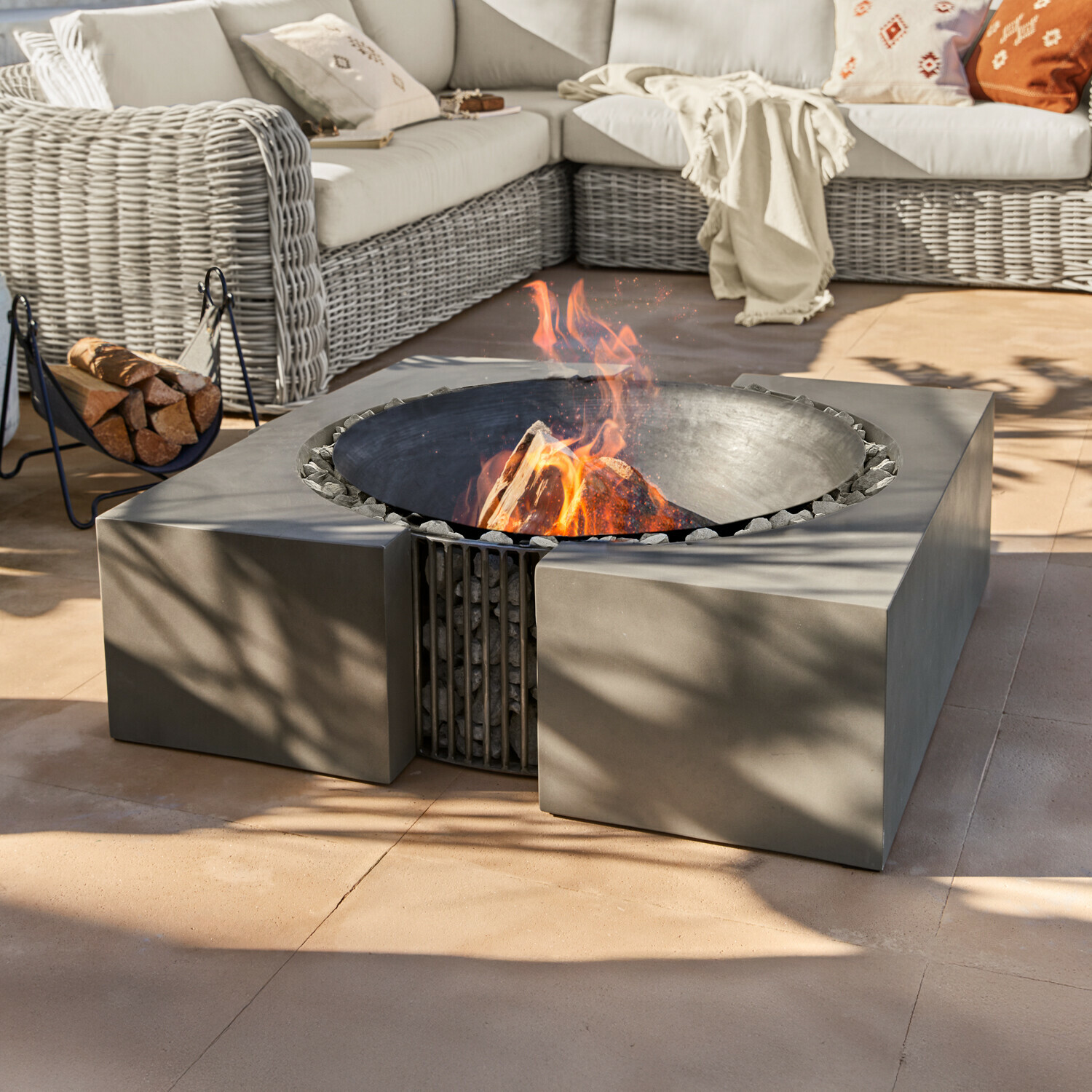Feuerstelle Charonville Modernes Feuerstelle aus schwarzem Metall mit Steinen auf Terrasse neben Rattansofa mit Kissen