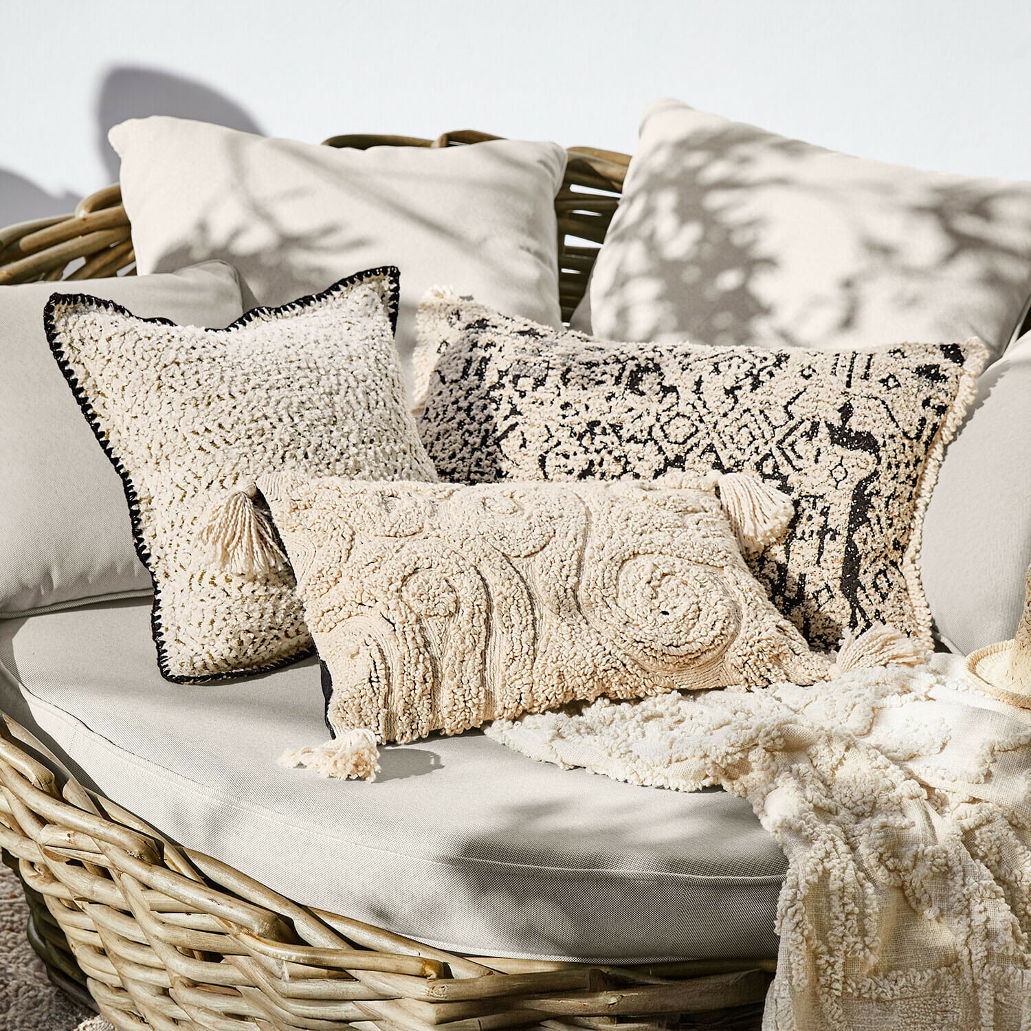 Set aus cremefarbenen Dekokissen aus weichem Material auf Rattansofa, Boho-Stil