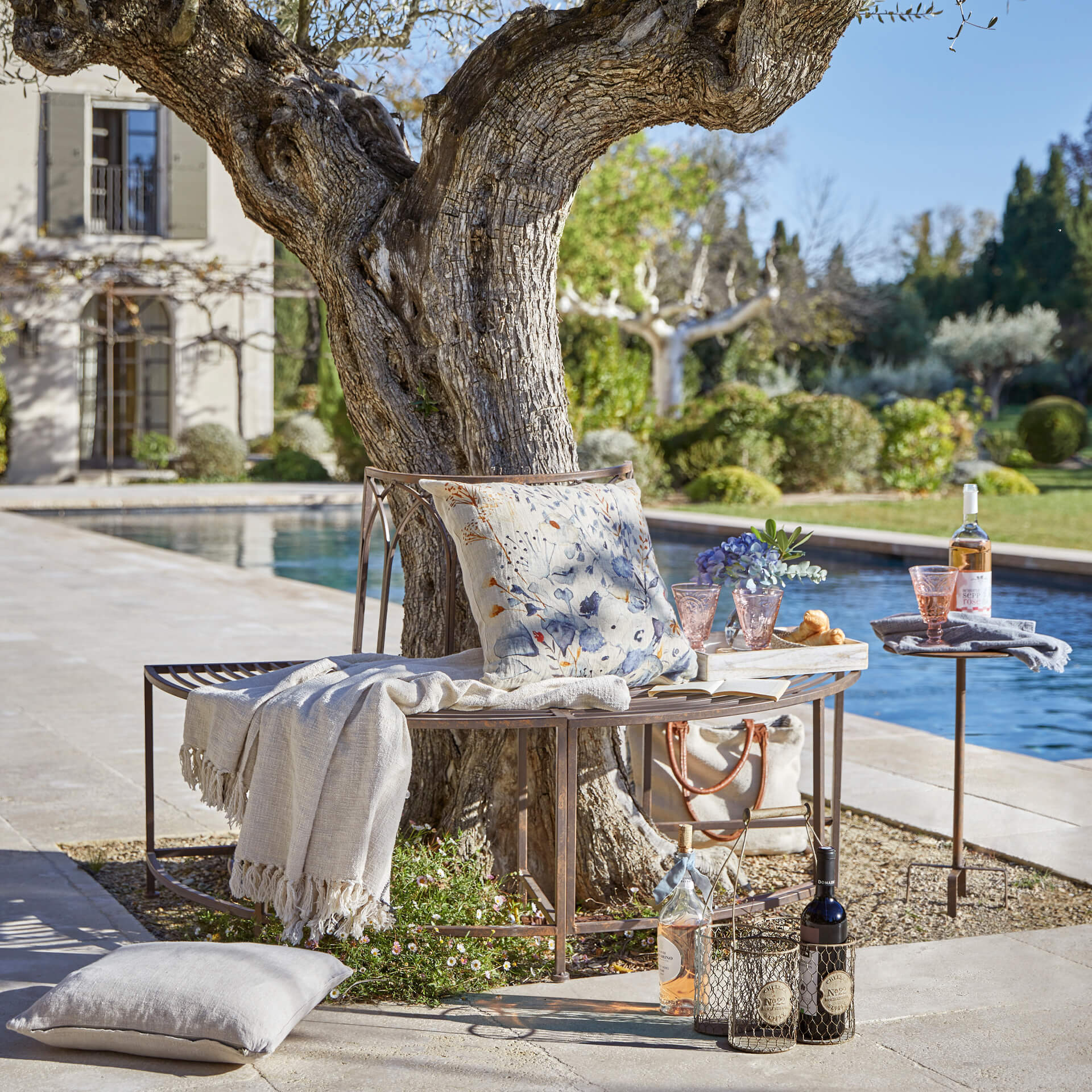 Metallbank in Kupferfarbe unter Baum mit Kissen und Decke am Pool im Garten