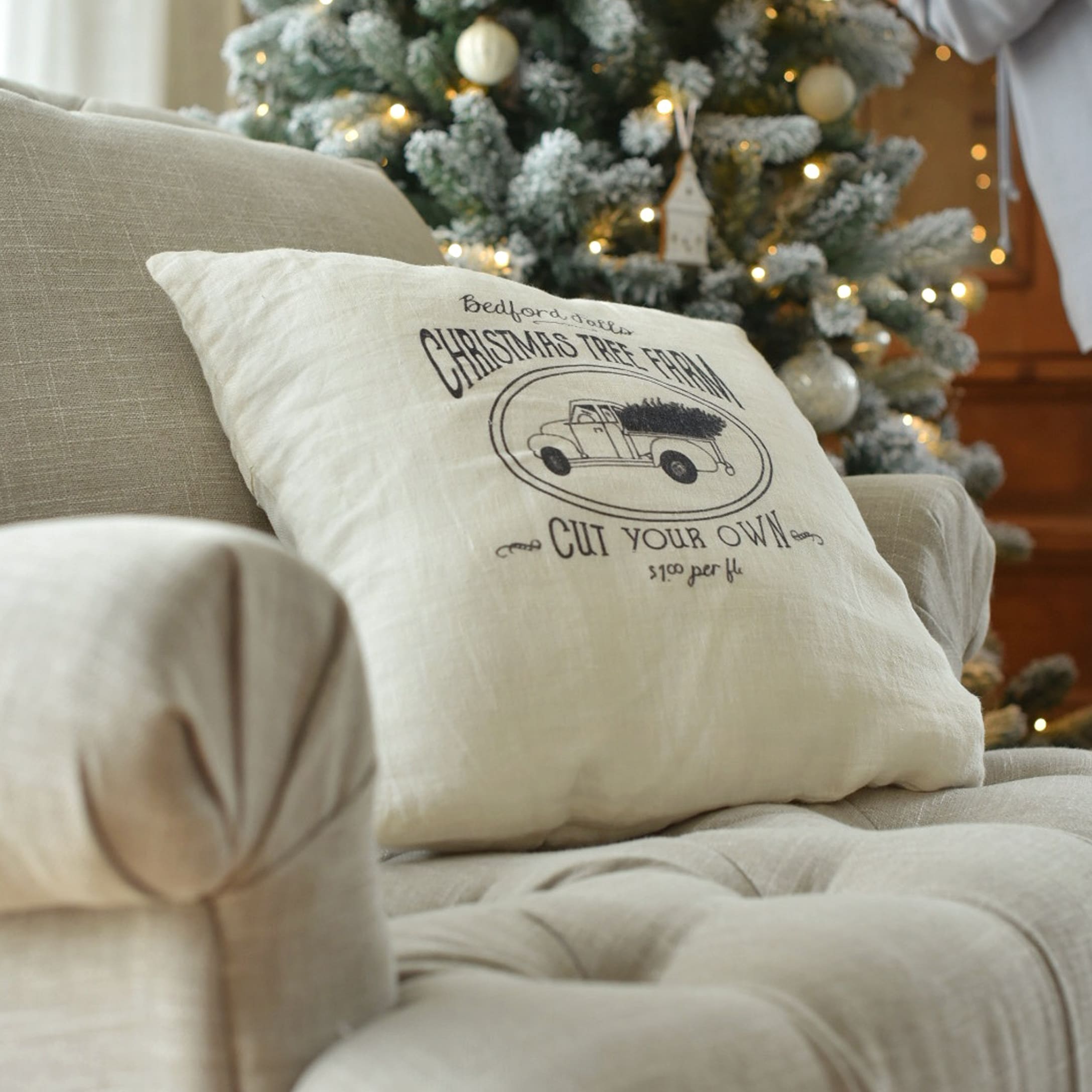 Beige Leinenkissen mit Weihnachtsauto-Aufdruck auf Sofa vor festlich geschmücktem Tannenbaum
