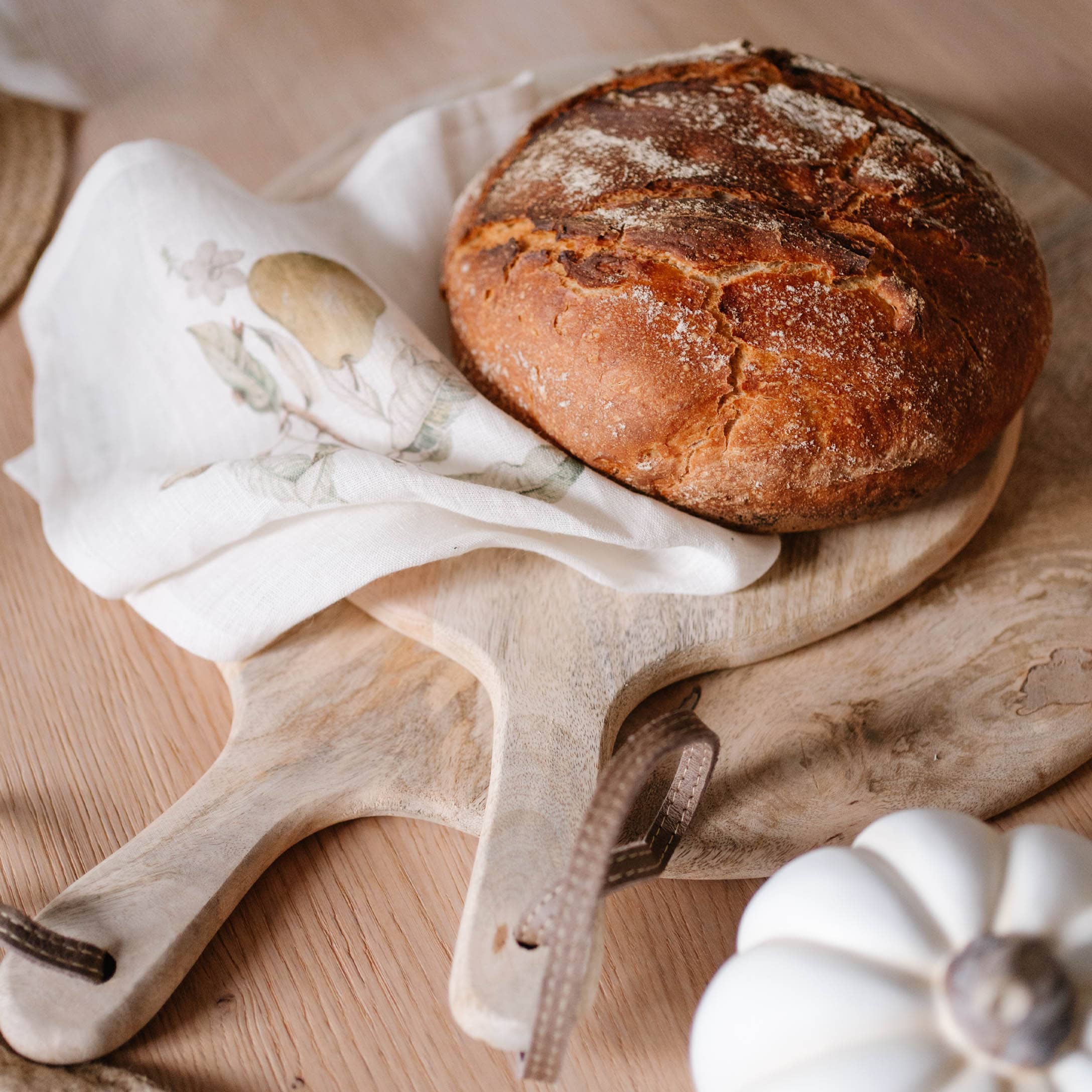 Frisches Brot auf Holzbrett mit Leinen-Tuch und weißem Deko-Kürbis auf Holztisch