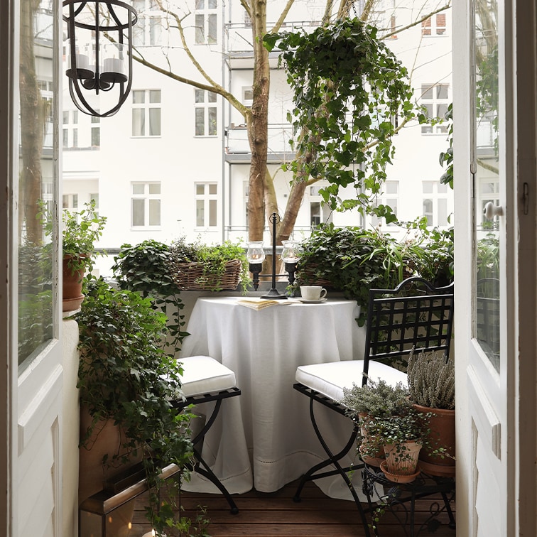 Gemütlicher Balkon mit weißem Tisch, schwarzen Stühlen und grünen Pflanzen zum Entspannen.