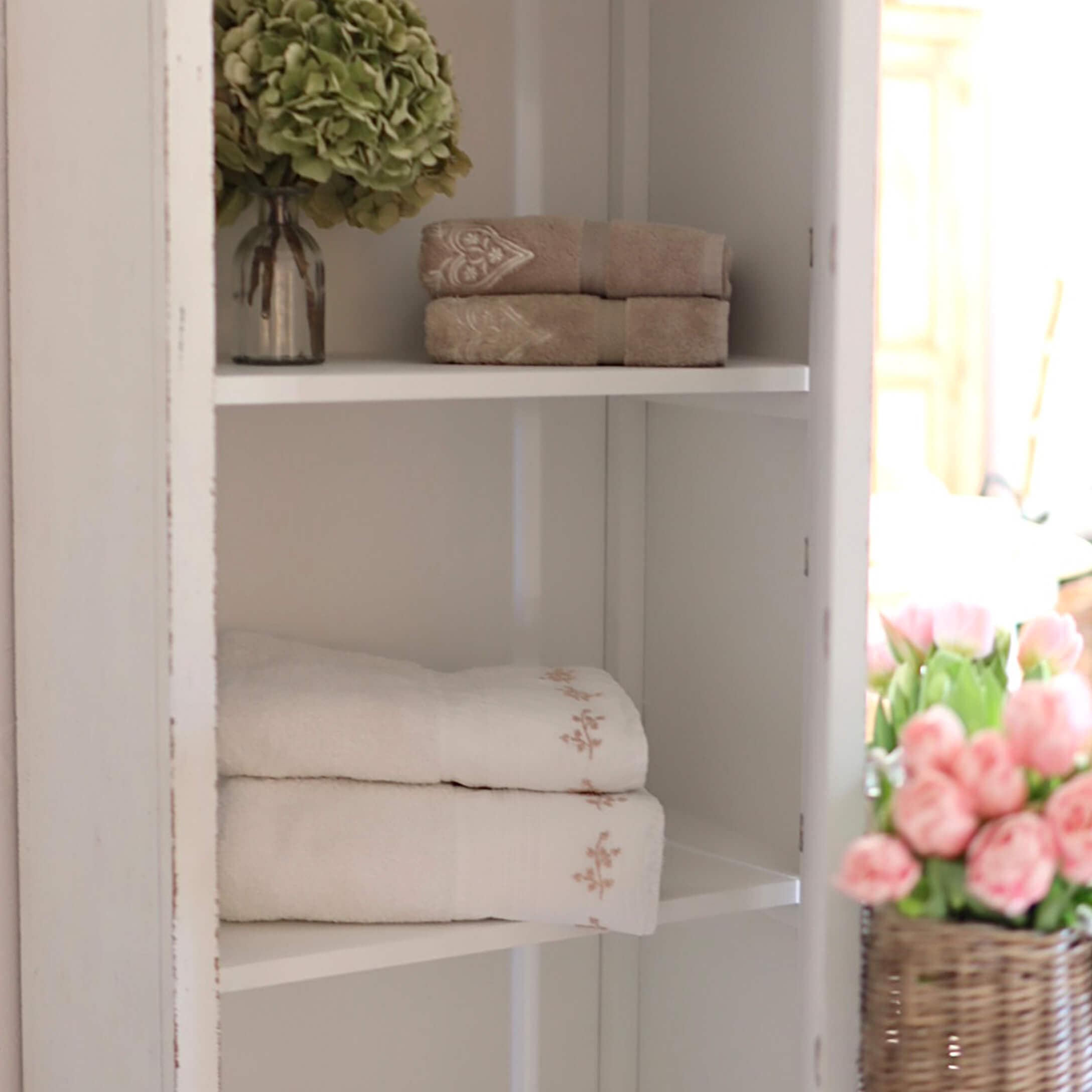 Weiche Baumwollhandtücher in Beige und Weiß mit feiner Stickerei auf weißem Regal