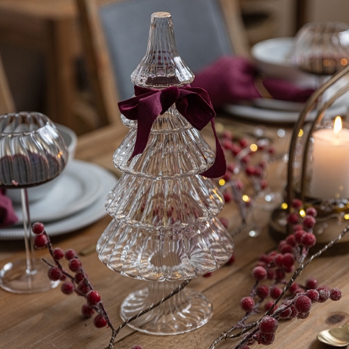 Glas-Weihnachtsbaum-Dekoration mit bordeauxroter Schleife auf Holztisch mit Weihnachtsdeko