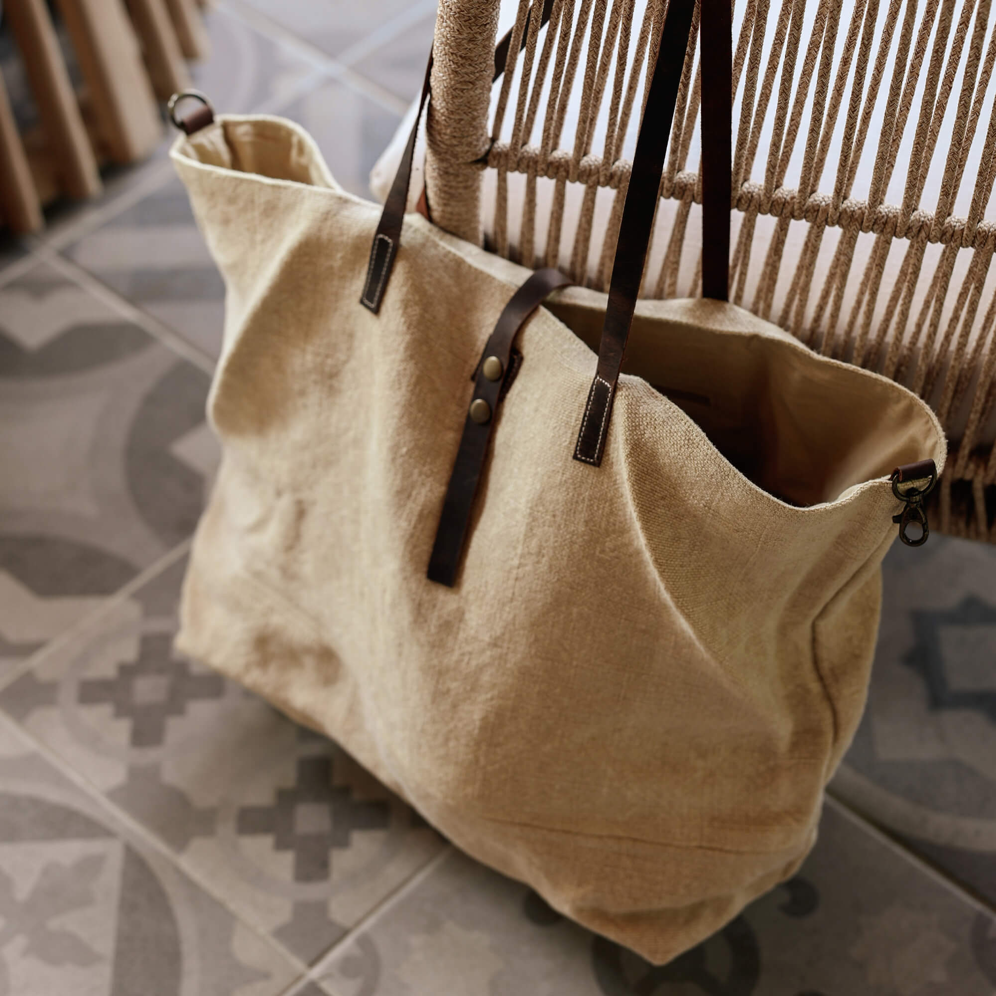 Beige Stofftasche mit dunkelbraunen Ledergriffen auf gemustertem Fliesenboden