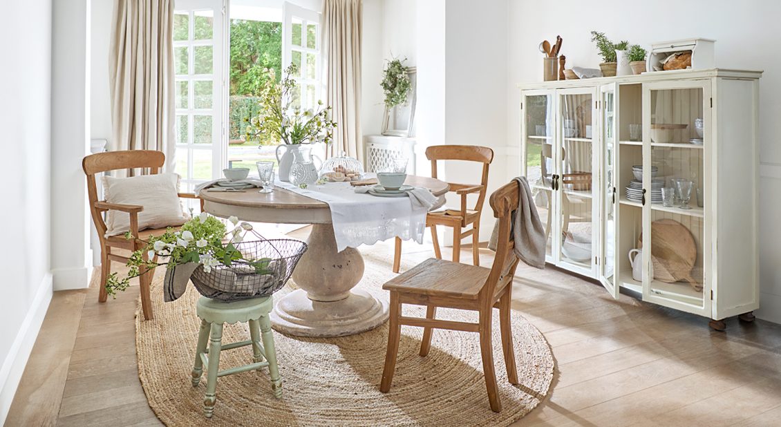 Helles Esszimmer mit rundem Holztisch, rustikalen Stühlen und natürlichem Teppich für gemütliche Atmosphäre