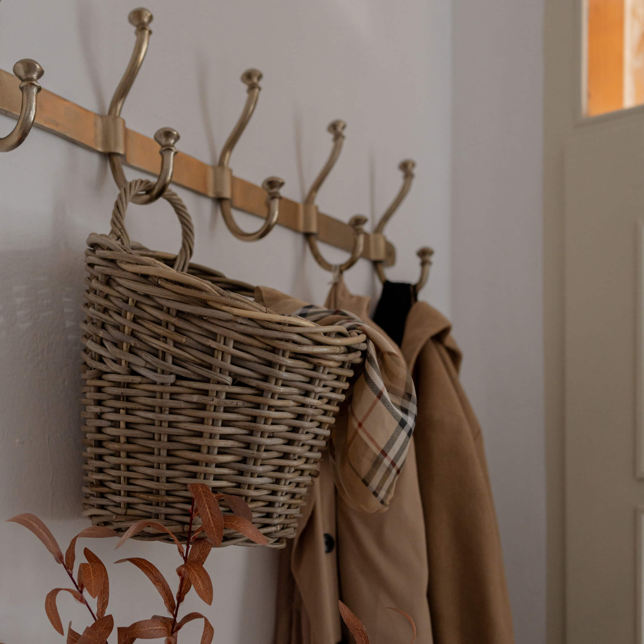 Geflochtener Korb aus Weide an Messinggarderobe mit beigem Mantel und kariertem Schal