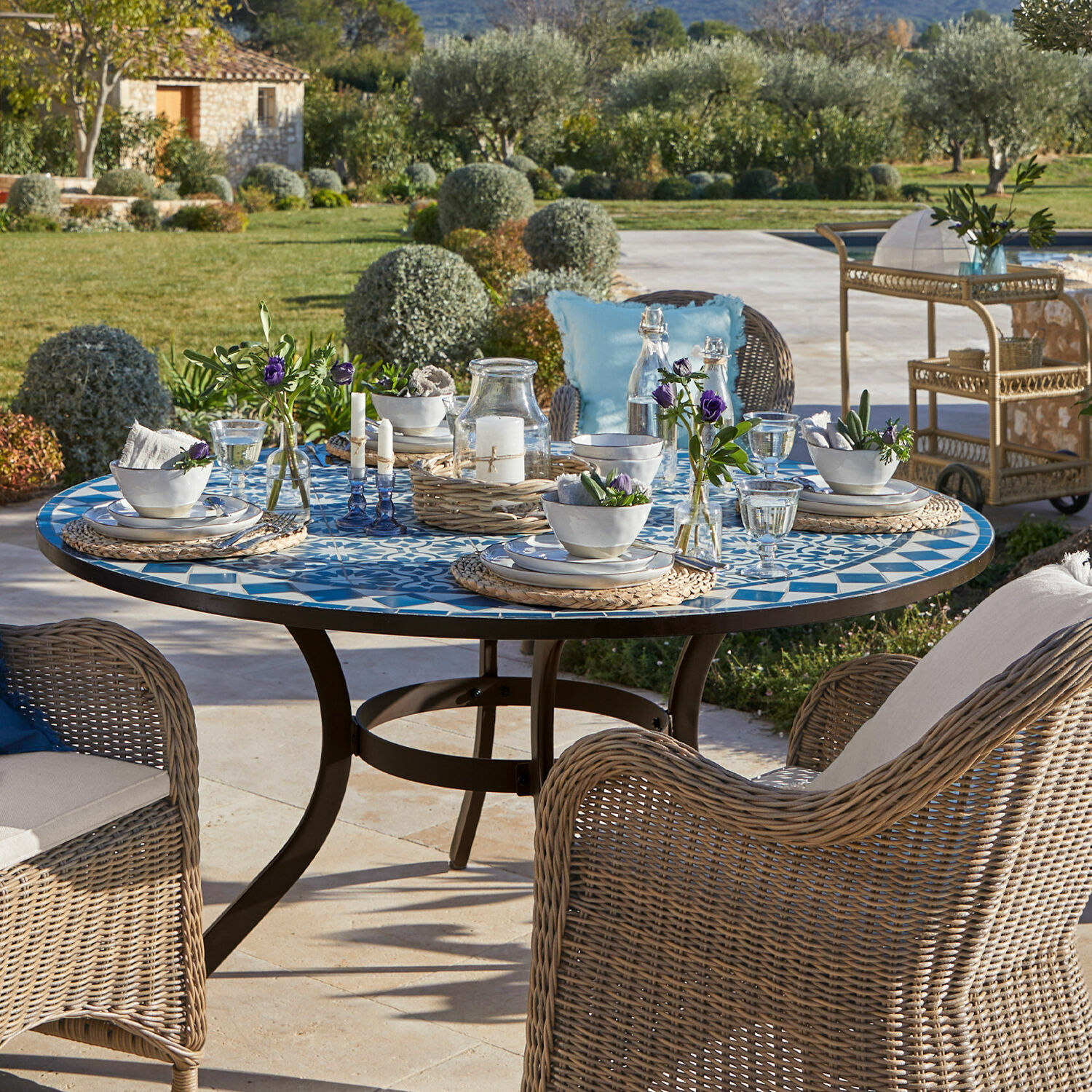 Tisch Jennarton Runder Gartentisch mit blau-weißem Mosaik-Tischplatte und Rattanstühlen auf der Terrasse