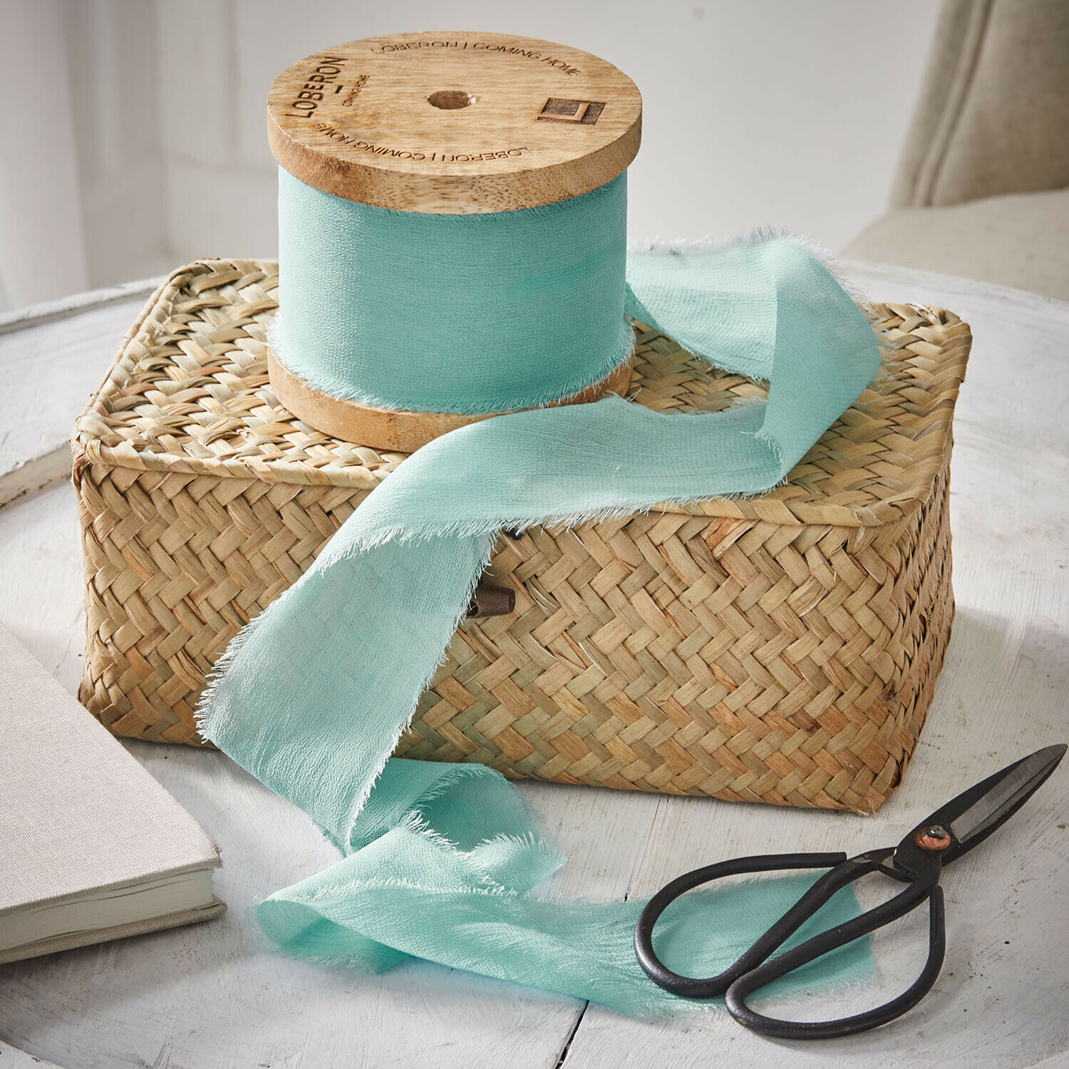 Mintgrünes Baumwollband auf Holzspule auf geflochtenem Korb mit schwarzen Scheren