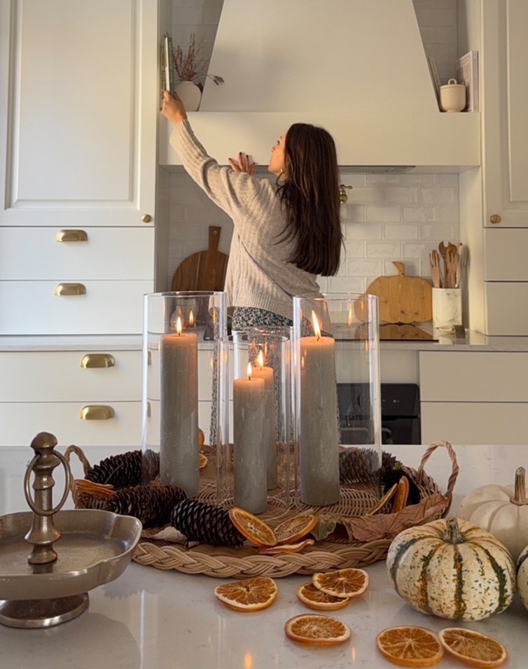 Herbstliches Dekorationsensemble mit grauen Kerzen, Kiefernzapfen und getrockneten Orangenscheiben auf Küchenarbeitsplatte