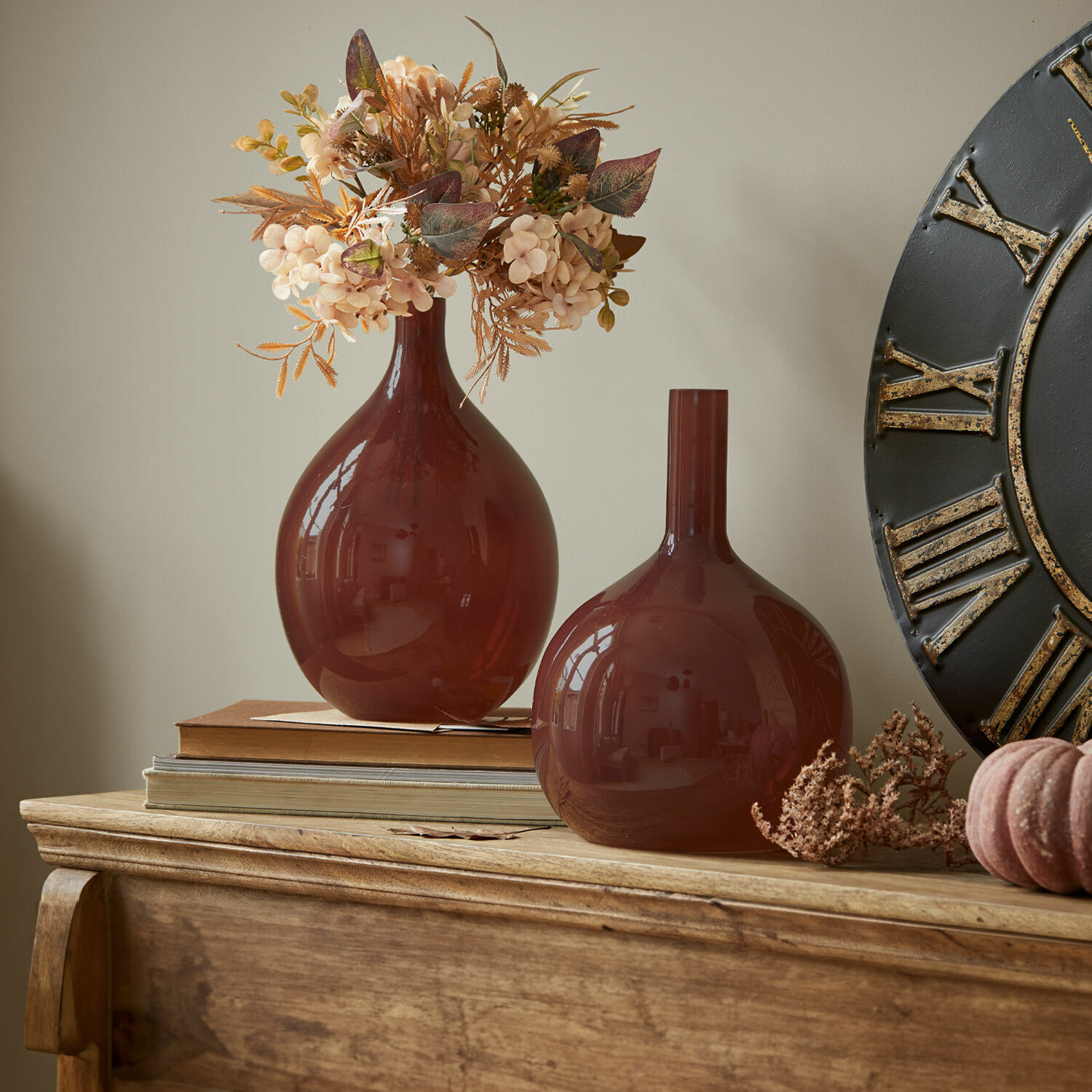 Zwei braune Glasvasen auf Holzkommode mit dekorativen Trockenblumen und Büchern
