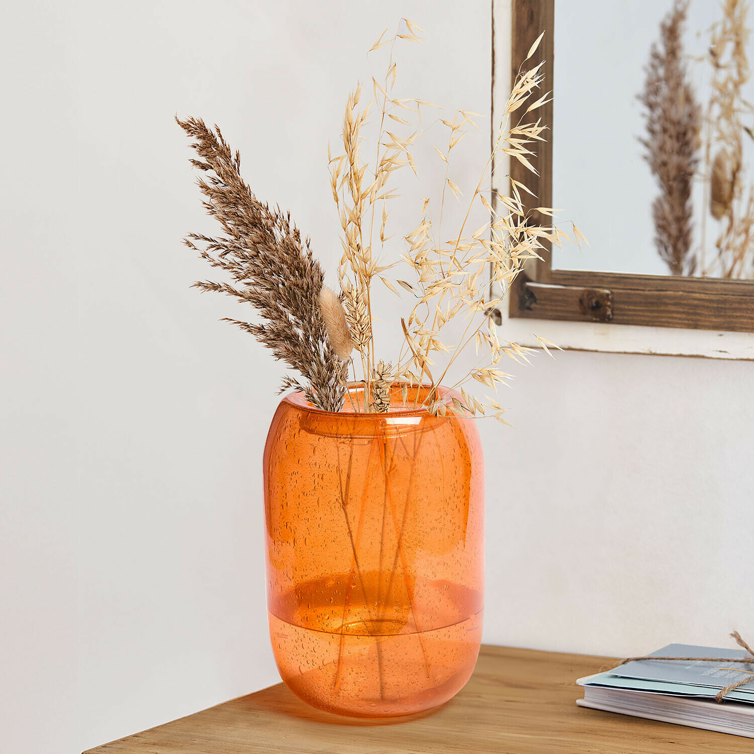 Orangener Glasvase mit Luftblasen und getrockneten Gräsern auf Holztisch als Wohnaccessoire