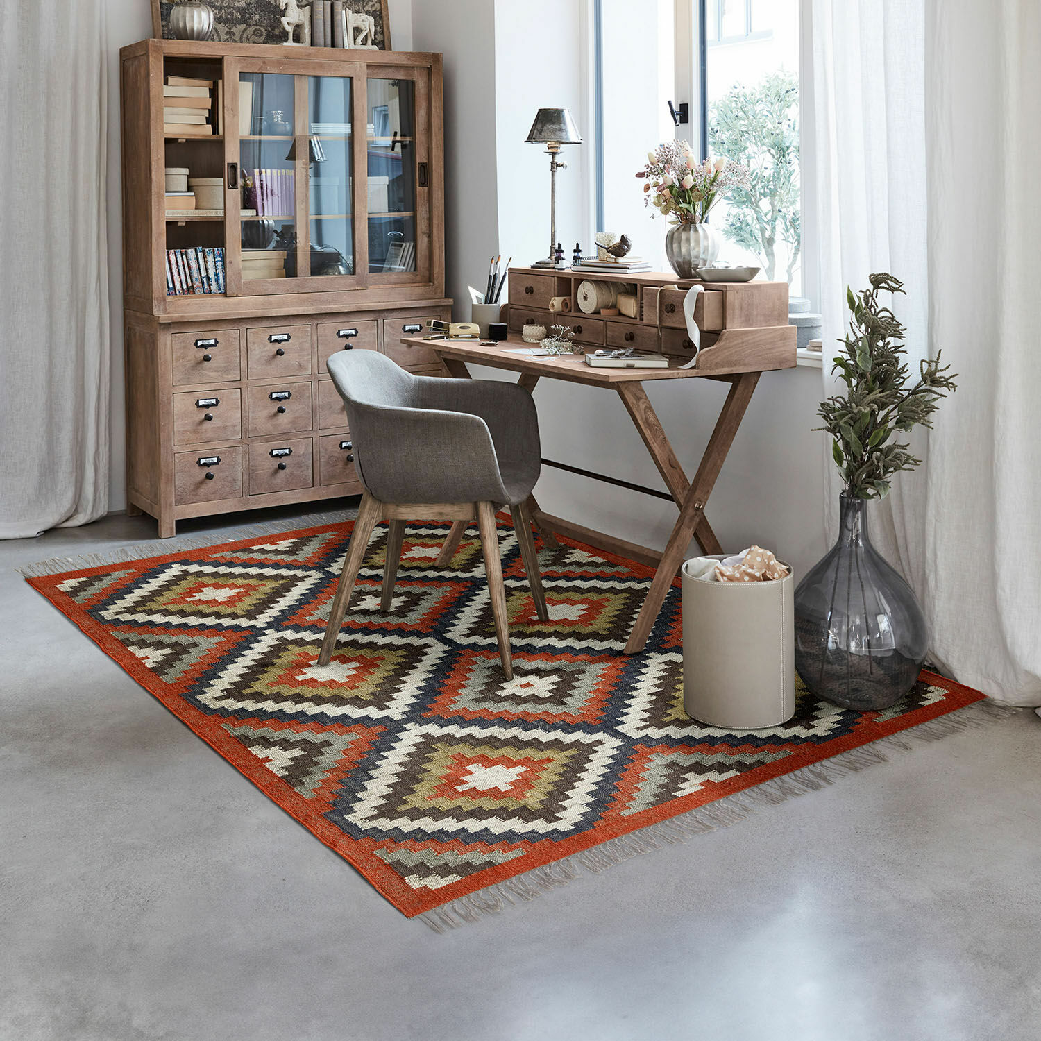 Geometrisch gemusterter Teppich in warmen Farben in modernem Arbeitszimmer mit Holzschreibtisch und grauem Stuhl