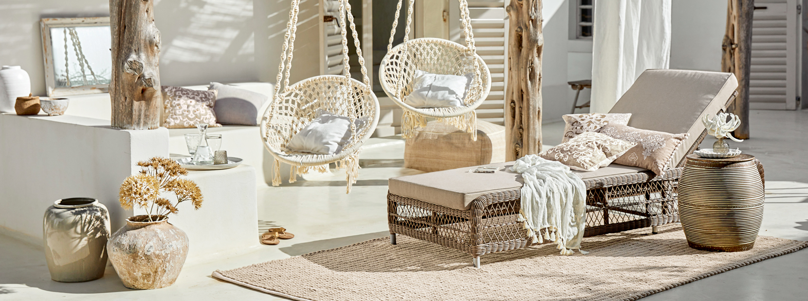 Gemütliche Lounge mit Rattan-Liegestuhl und hängenden Baumwollstühlen in Naturtönen