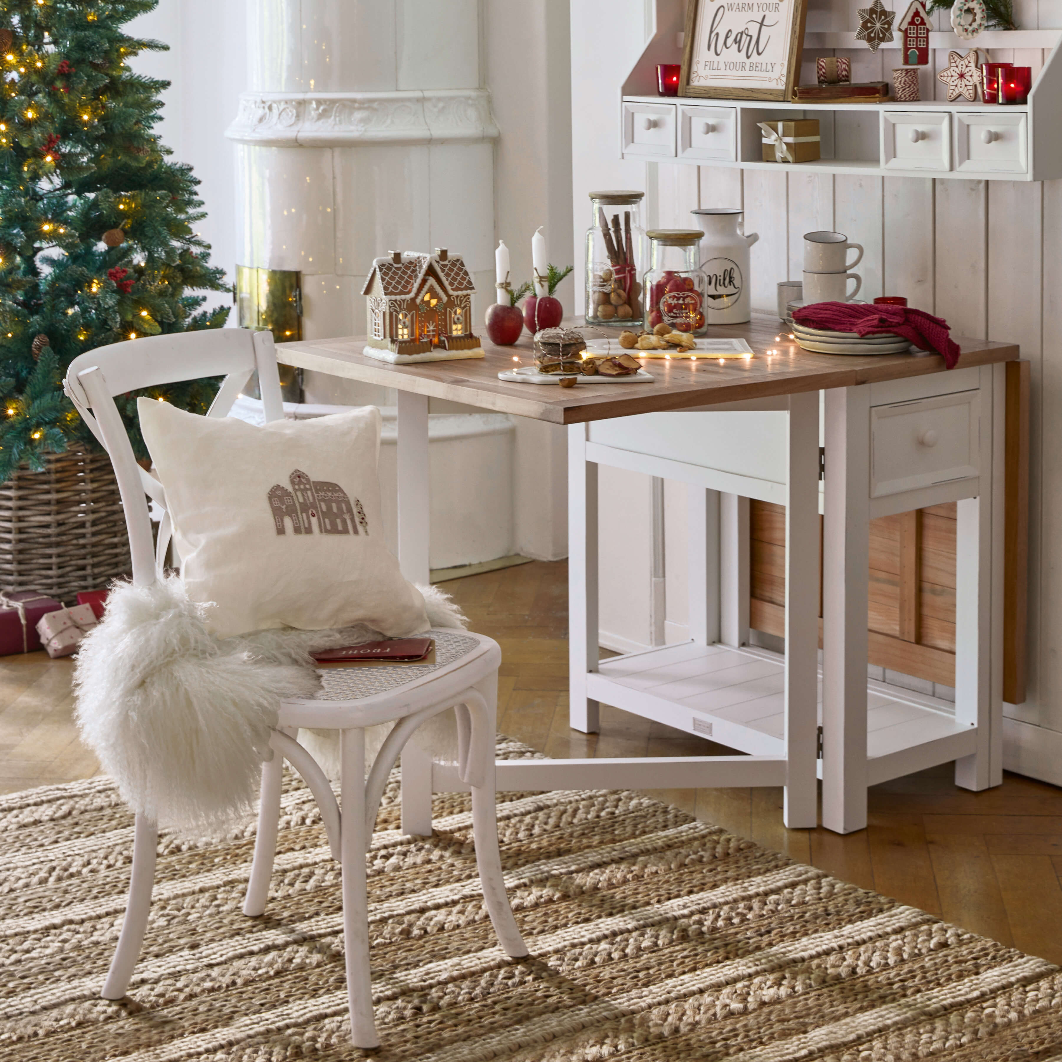 Gemütlicher weißer Holztisch und Stuhl mit Weihnachtsdekoration und beleuchtetem Tannenbaum im Hintergrund