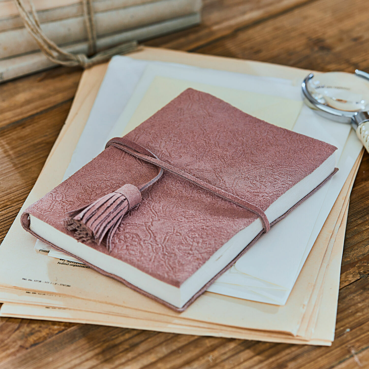 Notizbuch Orcival Rosa Notizbuch aus Wildleder mit Quaste auf Holztisch mit Dokumenten, Schreibzubehör