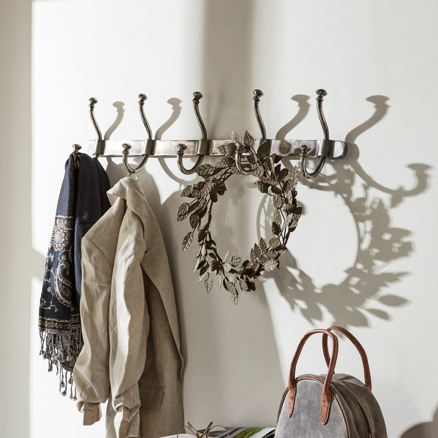 Hakenleiste Pincé Wandgarderobe aus Metall mit acht silbernen Haken, an denen Jacke und Schal hängen
