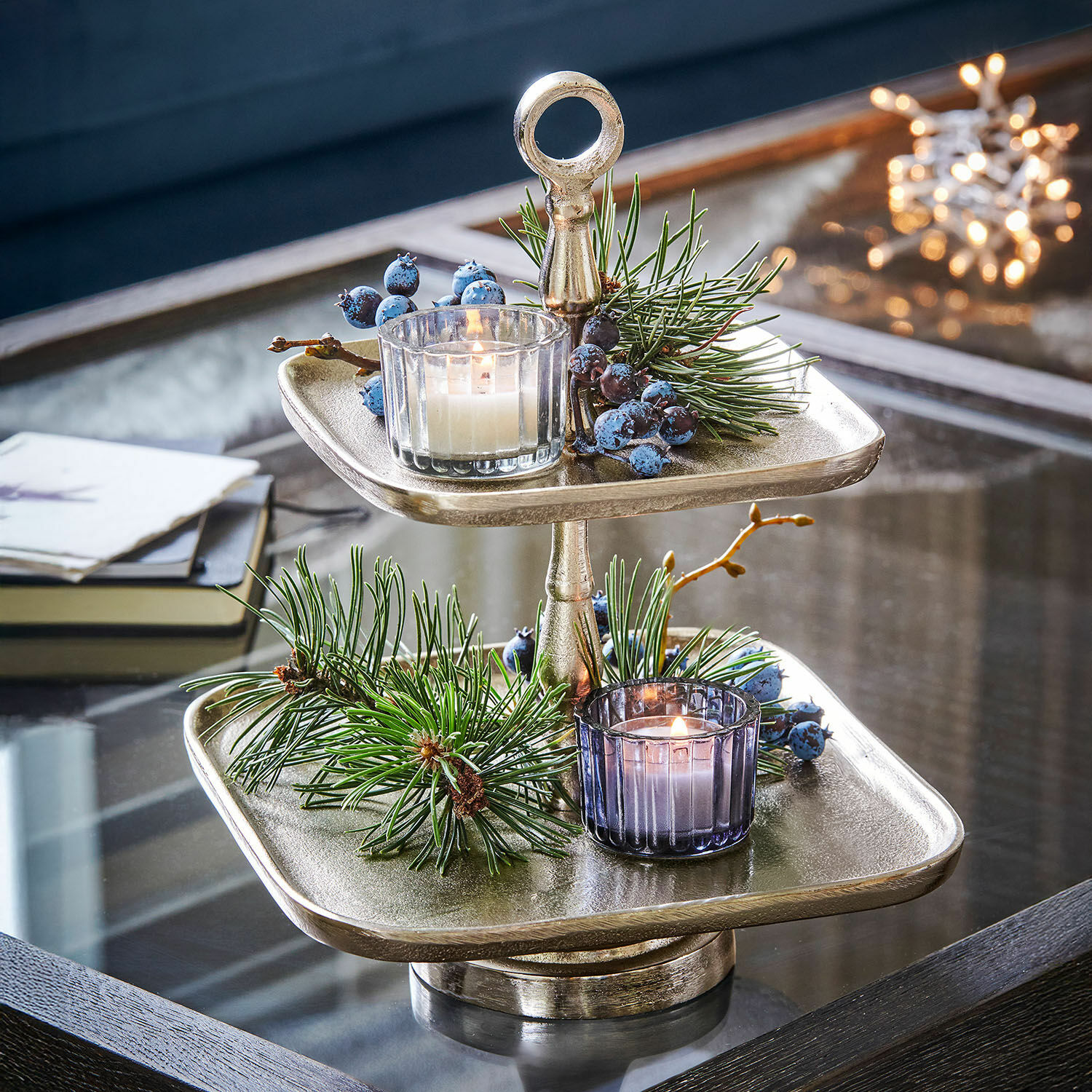 Zweistöckige silberne Metall-Etagere mit Weihnachtsdeko und Kerzen auf Glastisch