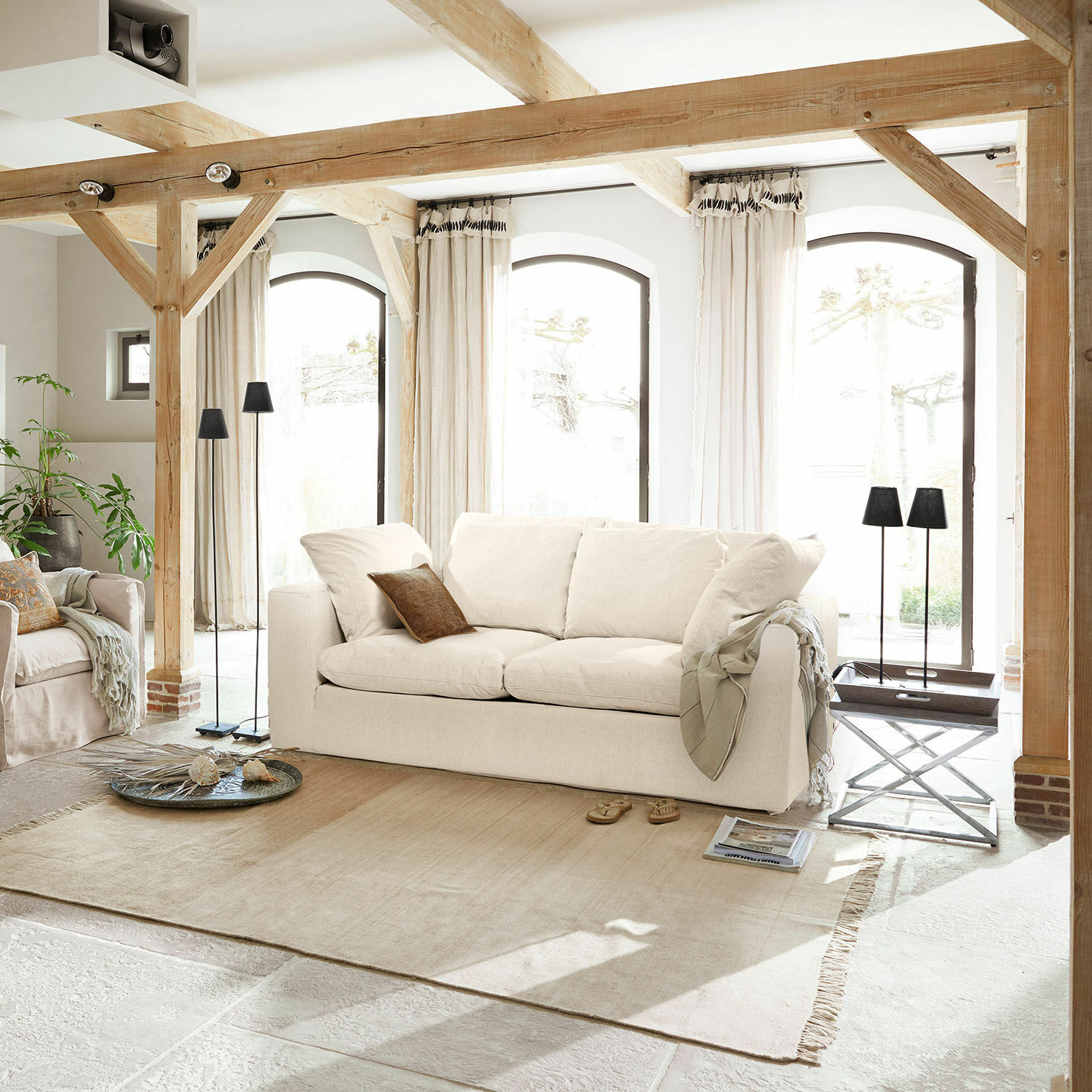 Sofa Xavreille Gemütliches hellbeiges Stoffsofa im hellen Wohnzimmer mit Holzbalken und hellem Teppich