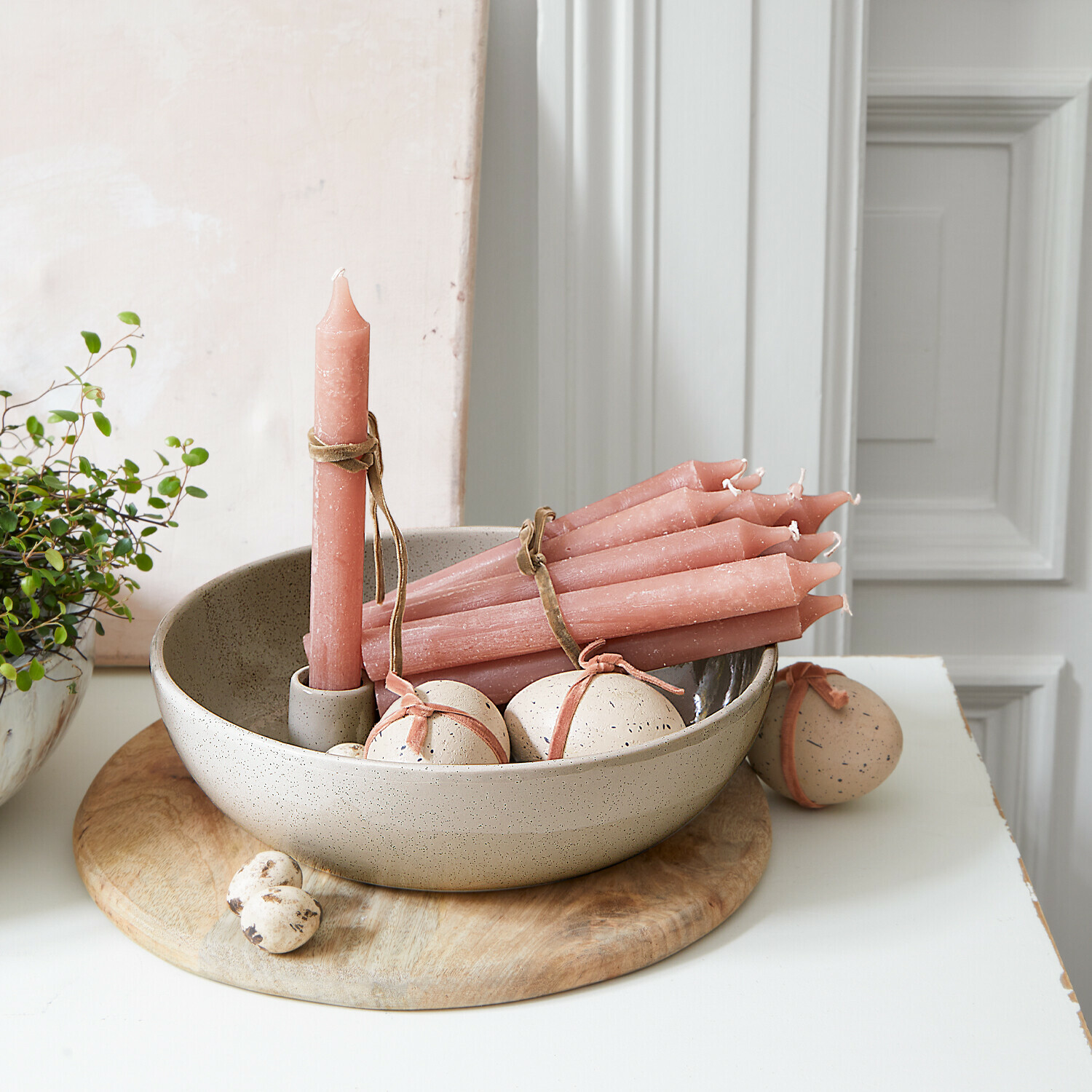 Set aus rosa Stabkerzen und dekorativen Eiern in Keramikschale auf Holzunterlage
