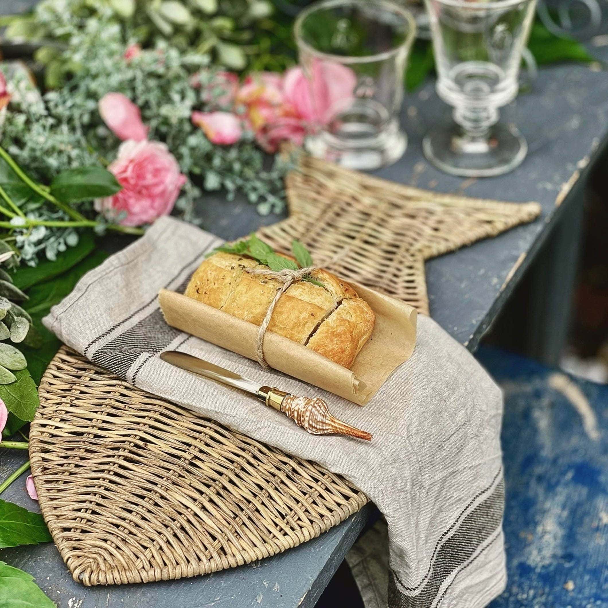 Rustikale Tischunterlage aus Seegras mit Brot und Muschelgriffmesser auf altem Tisch