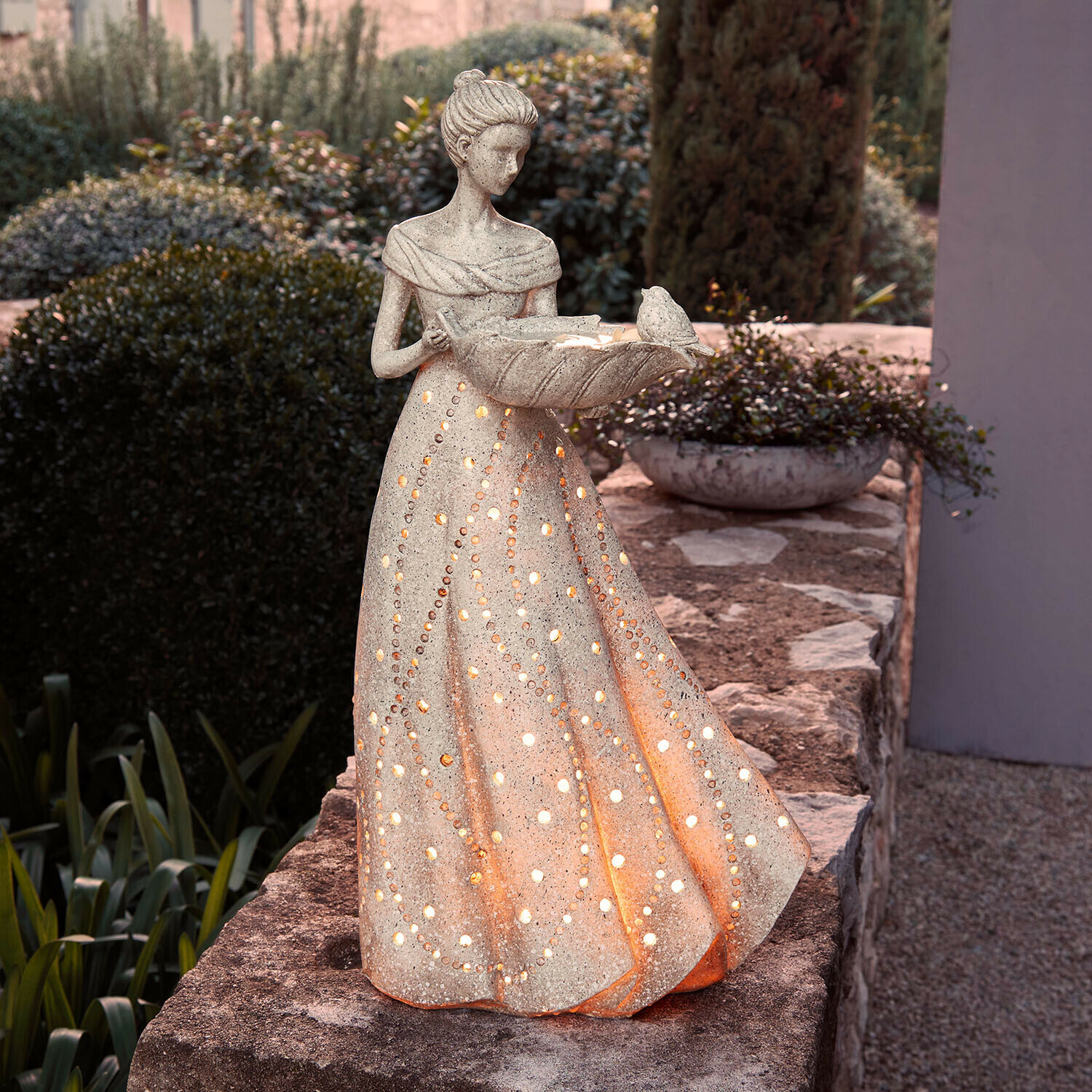 Beleuchtete Steinskulptur einer Frau im Kleid mit Löchern, Gartendekoration mit Vogel