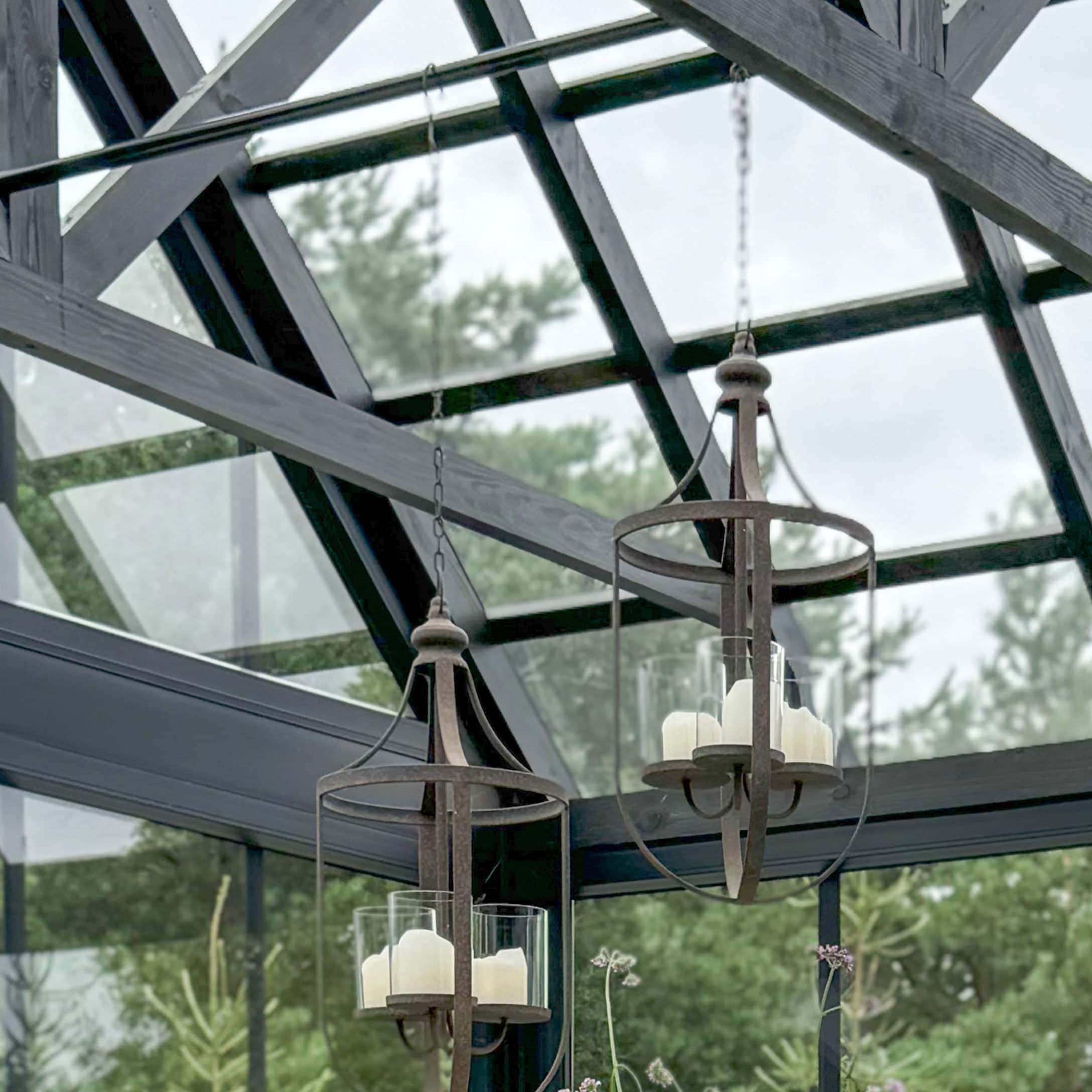 Hängende Laternen aus rostfarbenem Metall mit weißen Kerzen in einer hellen Orangerie