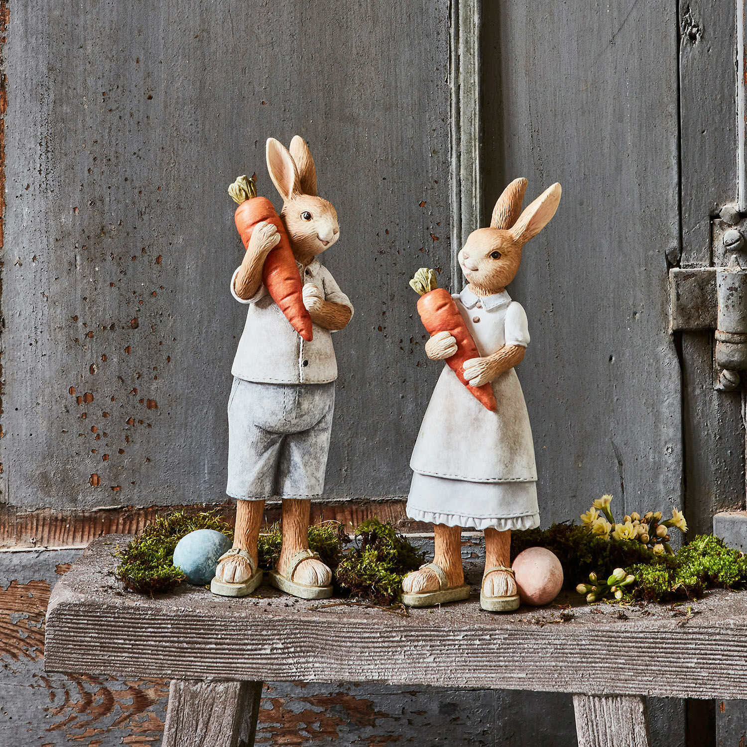 Hase 2er Set Gimont Figuren aus Material von Hasen in beiger Kleidung mit orangen Karotten auf rustikaler Holzbank