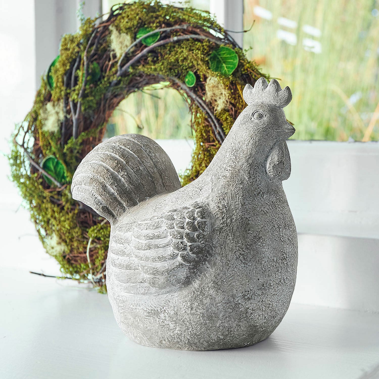 Deko-Henne Roselique Graue Hühnerfigur aus Beton als Dekoration vor hellem Hintergrund mit grünem Kranz