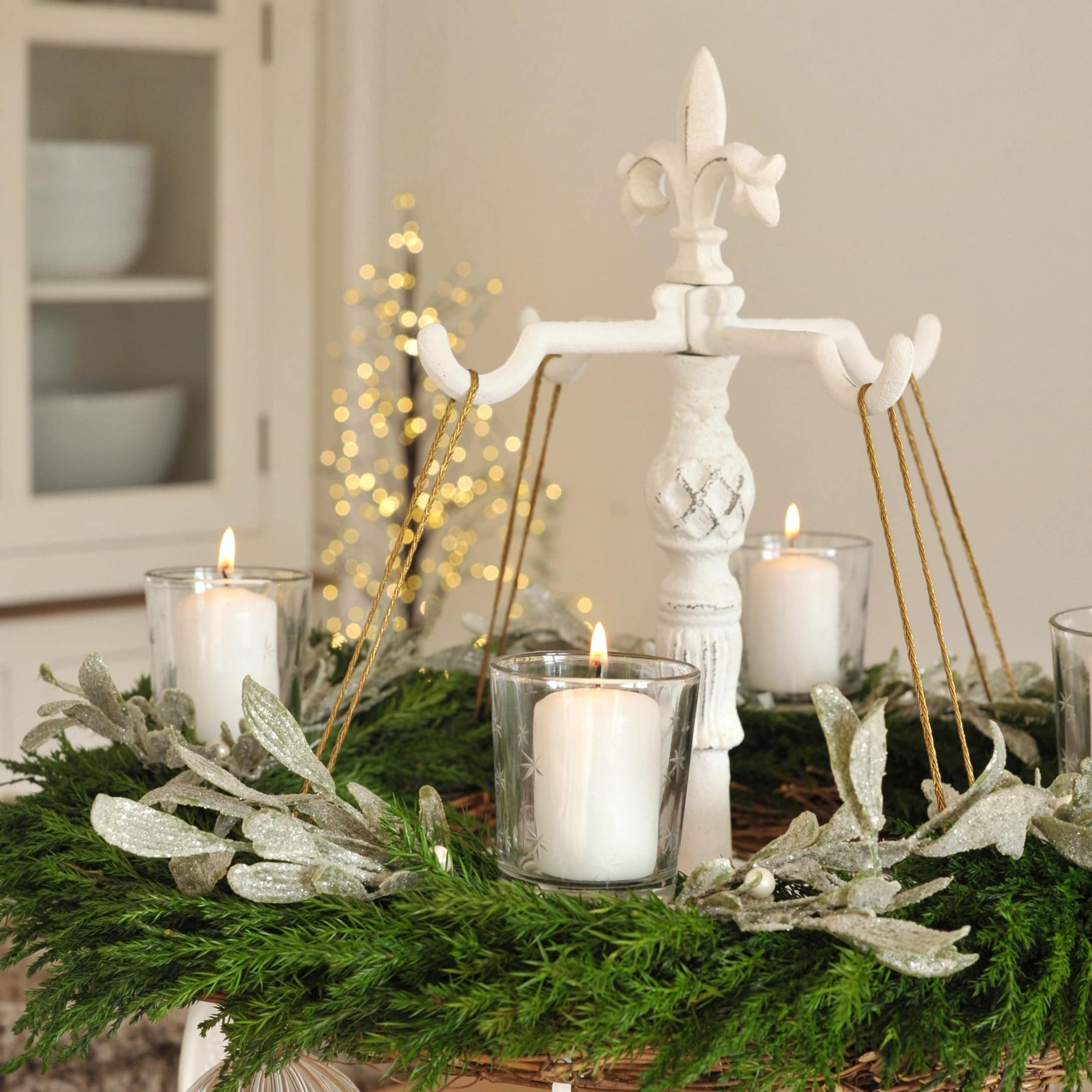 Weißer Metallständer mit grünem Adventskranz und brennenden Kerzen in Glasbehältern