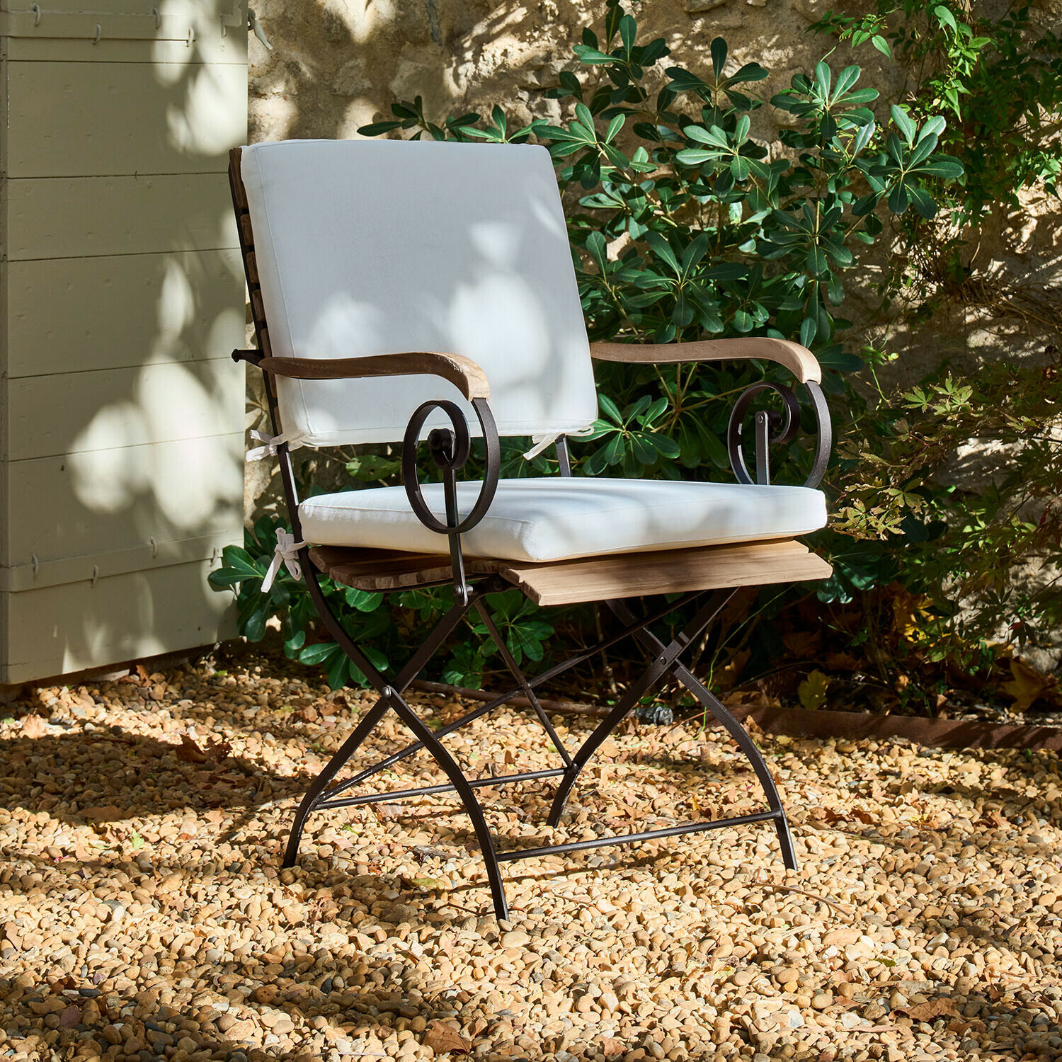Gartenstuhl mit Metallgestell, Holzarmlehnen und weißem Polster auf Kiesboden