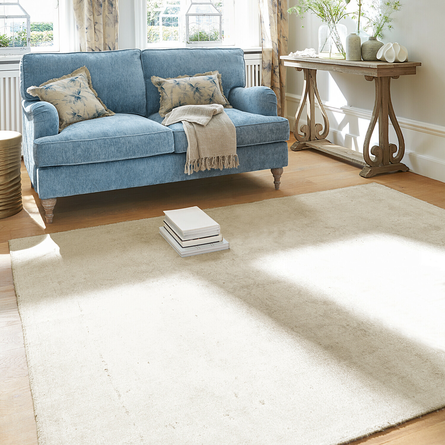 Hellblaues Stoffsofa mit beiger Decke und Kissen, cremefarbener Teppich in hellem Wohnzimmer