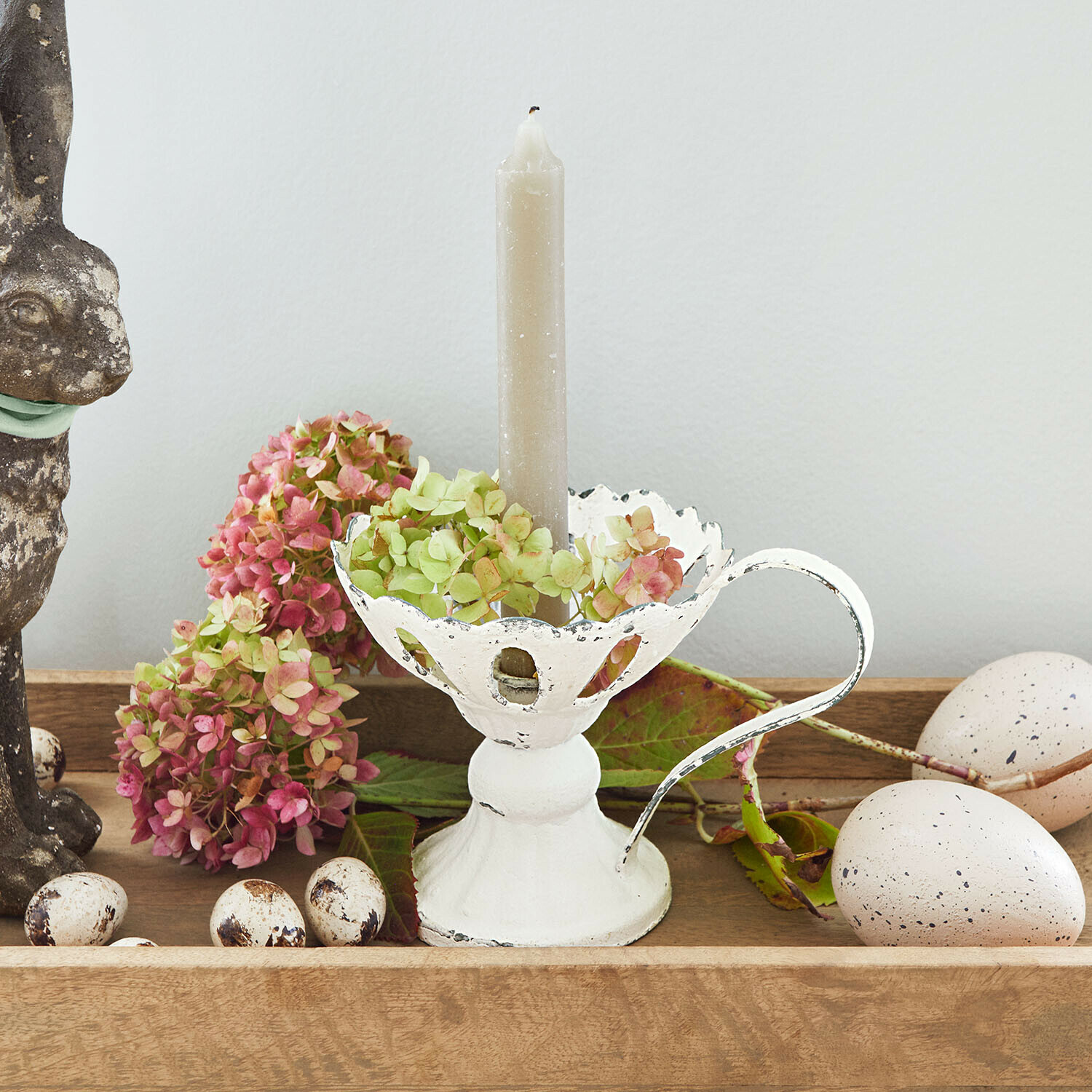 Weißer Metall-Kerzenhalter mit Griff und grauer Kerze, dekoriert mit Blumen und Deko-Eiern