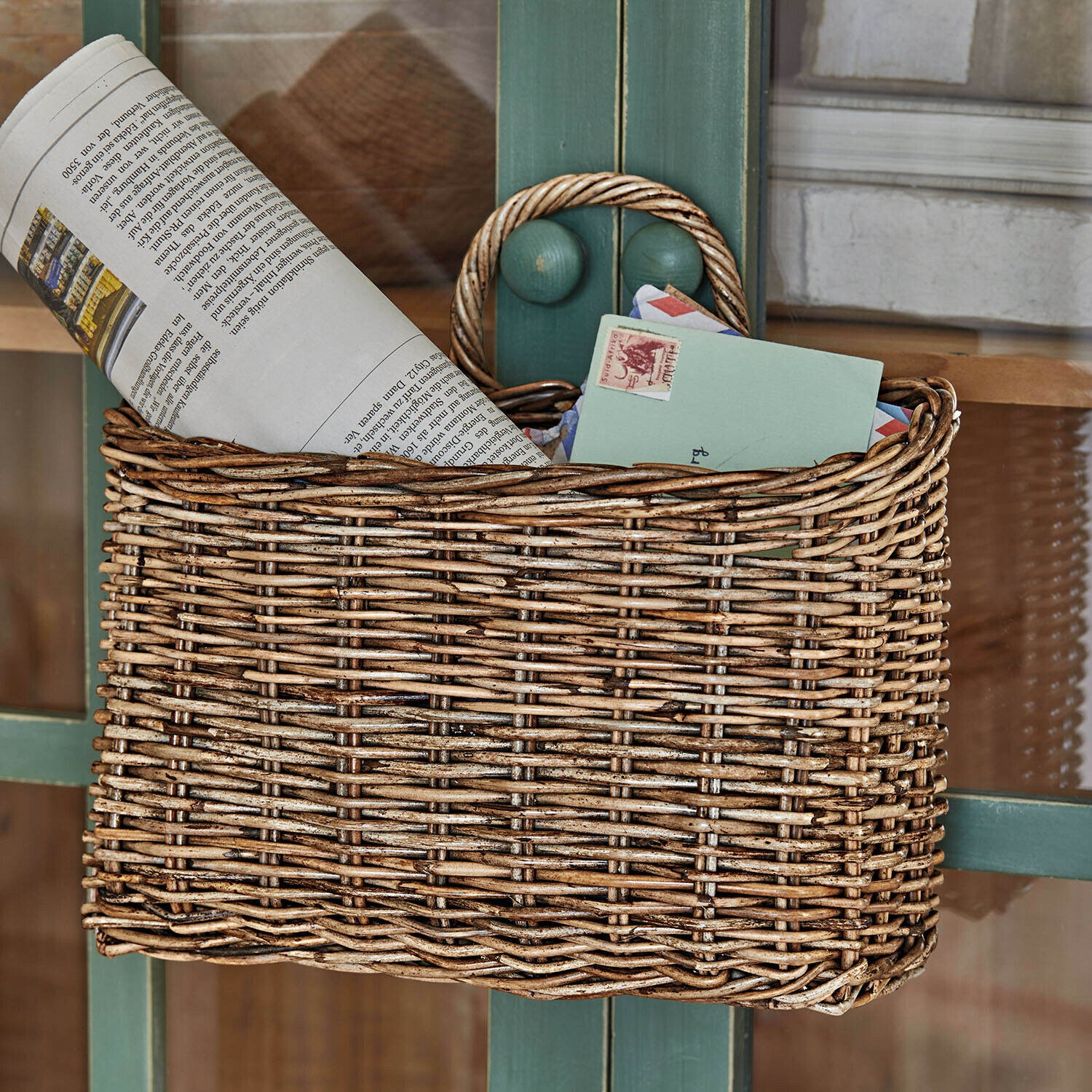 Naturfarbener Korb aus Weide für Briefe und Zeitungen an grüner Tür hängend