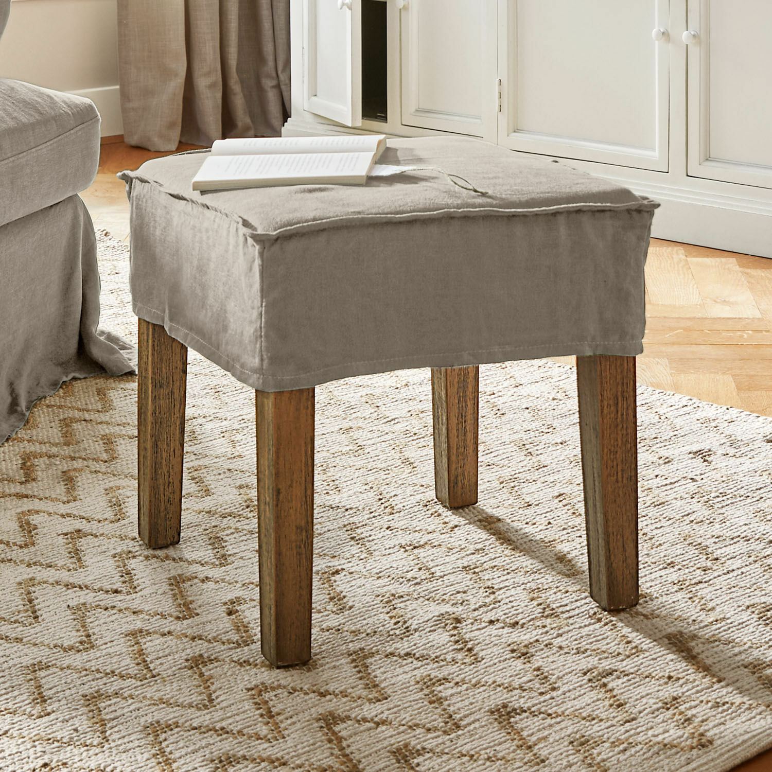 Hocker Vionnique Beiger Hocker mit Baumwollbezug und Holzbeinen auf hellem Teppich im Wohnzimmer