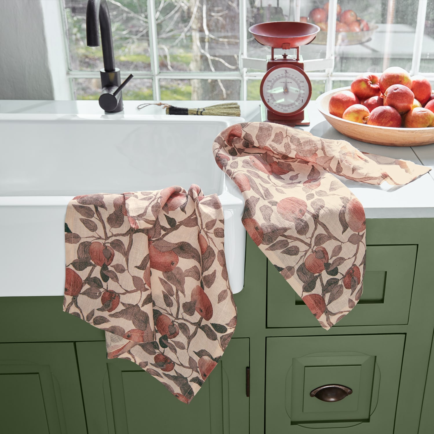 Leinen-Geschirrtücher mit Apfelmuster in warmen Farben auf grünem Küchenschrank