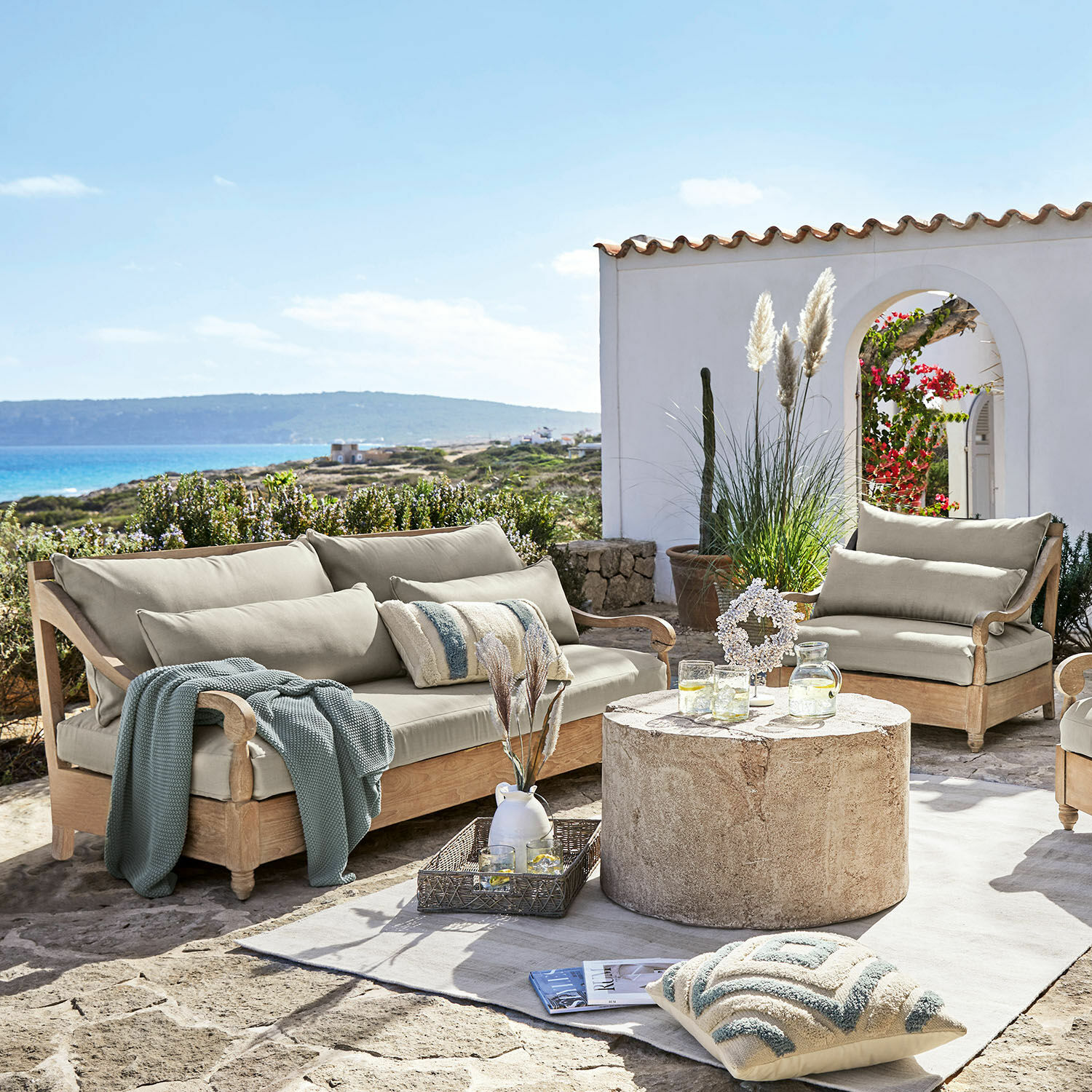 Sitzgruppe Montcassin Gartenmöbel-Set aus hellem Holz mit beigen Polstern auf steinerner Terrasse mit Meerblick