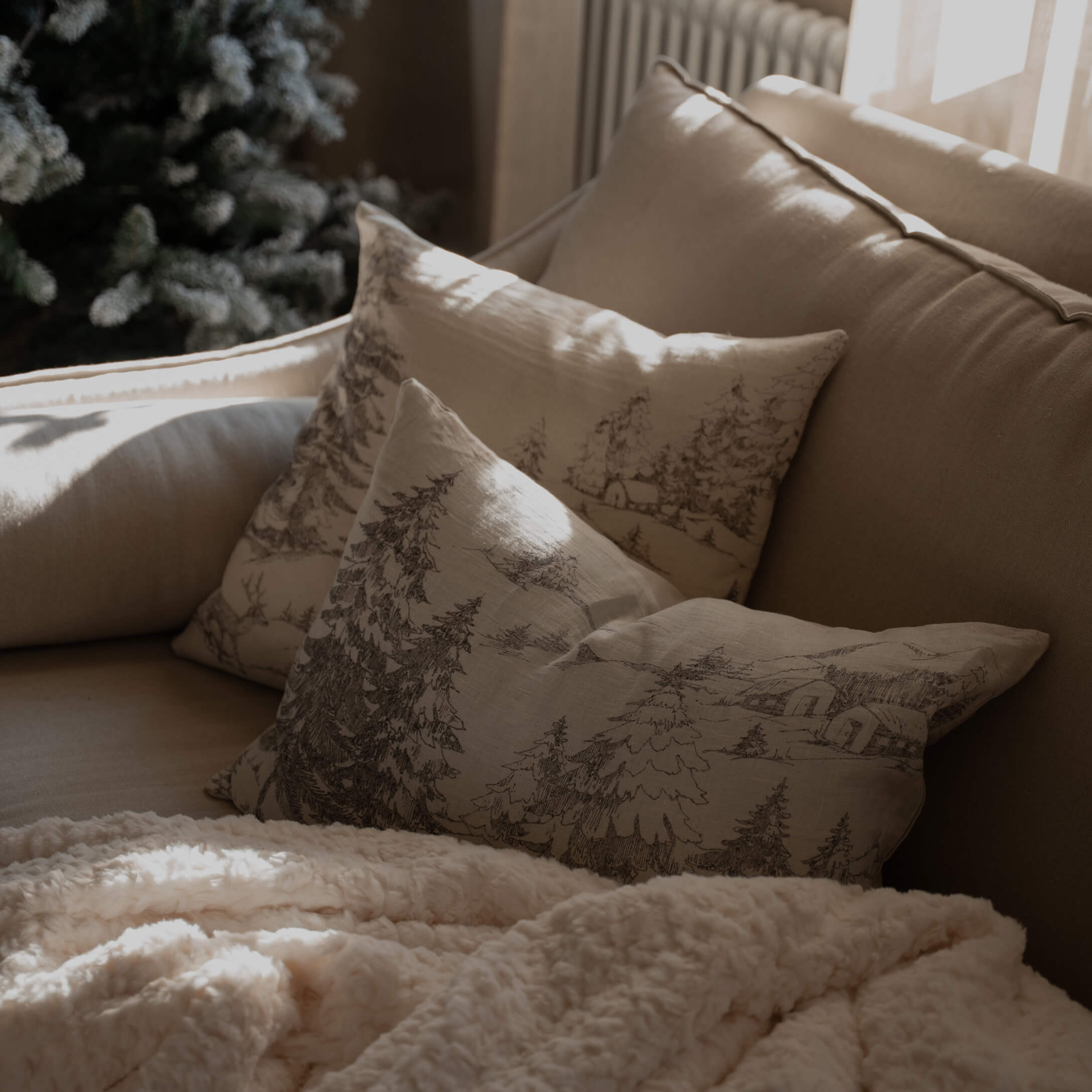 Beiges Sofa mit Waldmuster-Kissen und weicher cremefarbener Decke für gemütliches Wohnzimmer