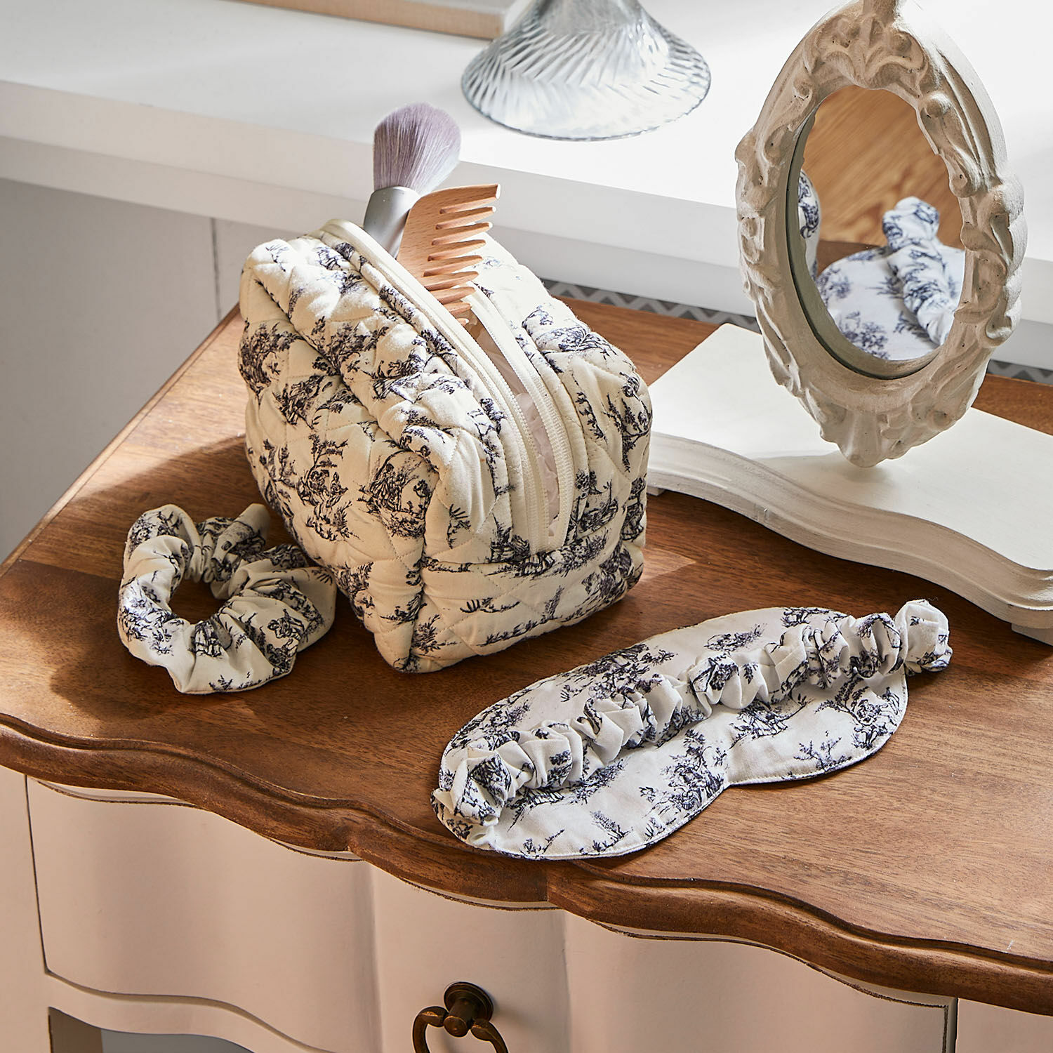 Beige gesteppte Kosmetiktasche mit schwarzem Muster, Haarband und Schlafmaske auf Holzplatte, Pflegeaccessoires