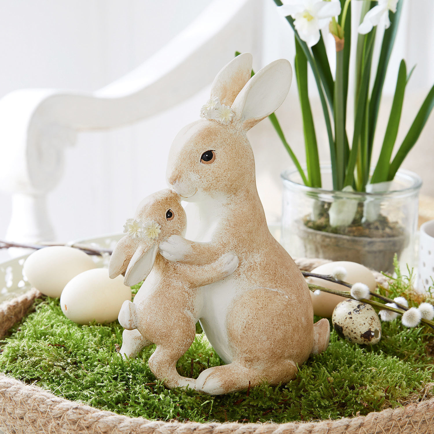 Hasen Aliena Figuren von zwei beige-weißen Hasen mit Blumenkränzen auf grünem Moos, österliche Dekoration