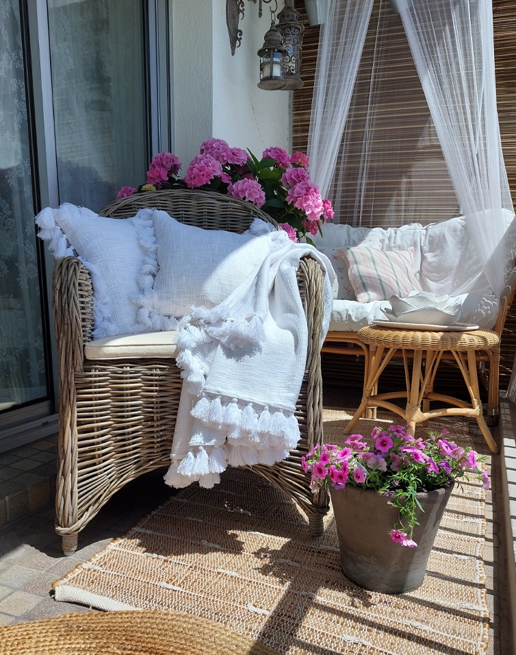 Gemütlicher Balkon mit Rattansessel, weißer Decke und pinken Blumen, natürliche Dekoration