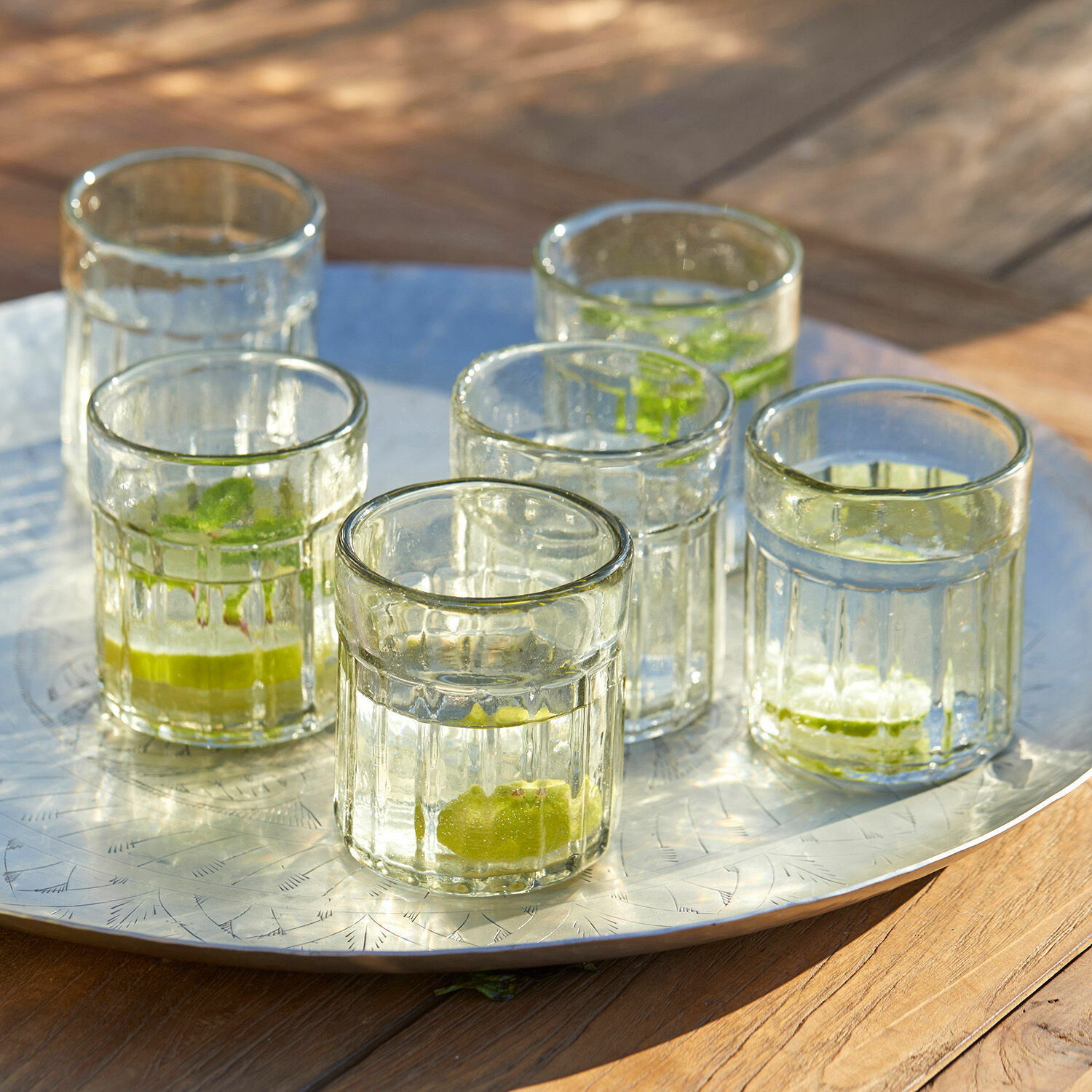 Glas 6er Set Roseville Sechs durchsichtige Gläser mit Limettenstücken auf einer Metallplatte auf Holztisch