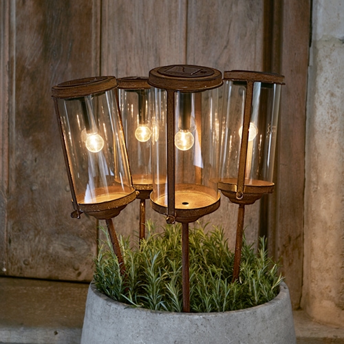 Set aus vier Gartenlampen aus Glas und rostigem Metall in einem Topf mit grünen Pflanzen, dekorative Außenbeleuchtung